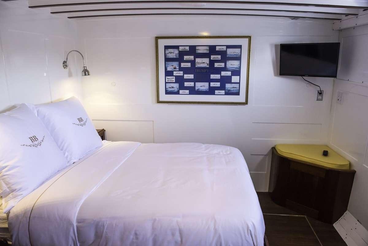 a bed with a white pillow and a television on the wall aboard BB Yacht for Charter
