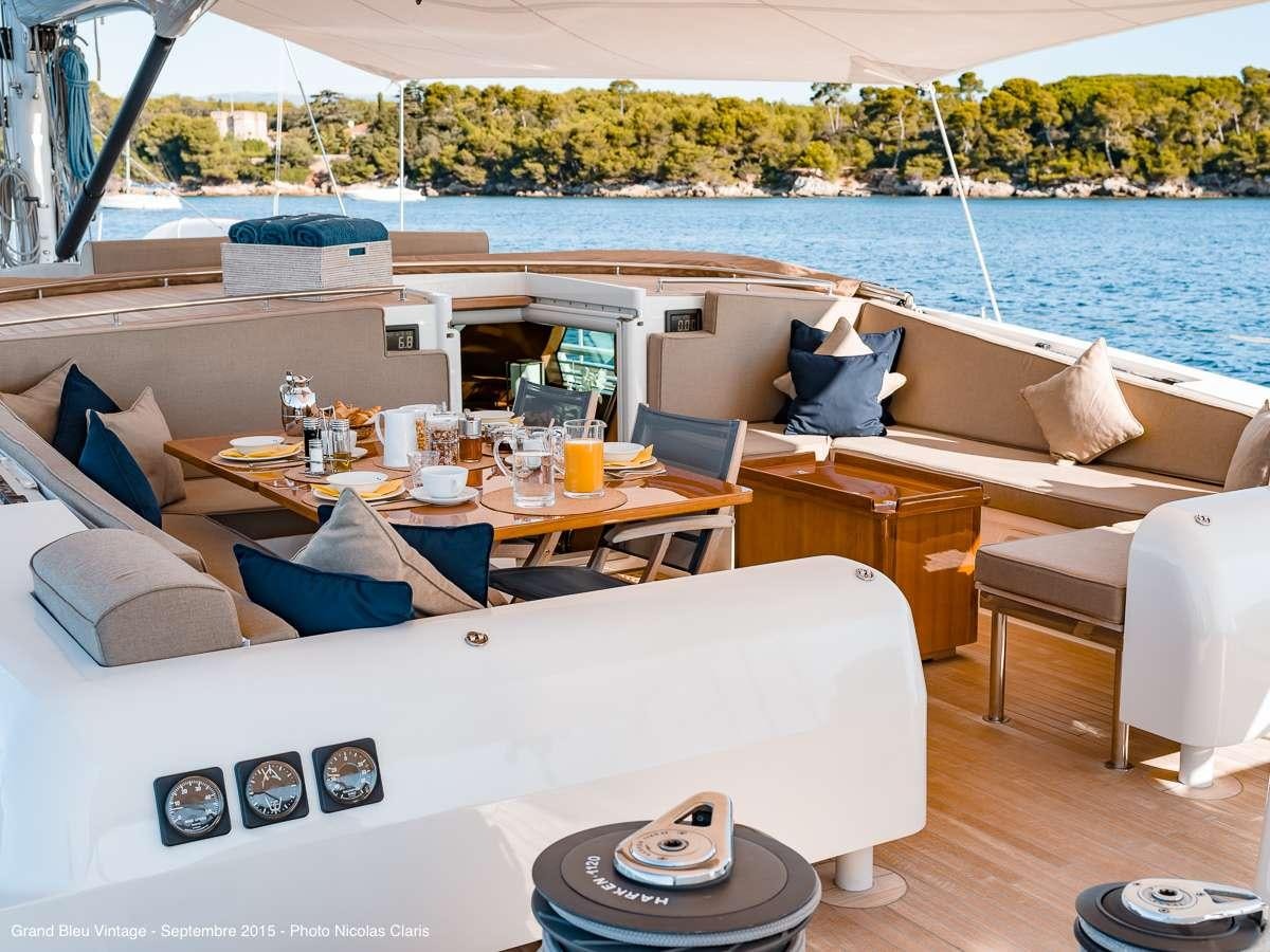 a room with a bed and a table with chairs and a large body of water in the background aboard GRAND BLEU VINTAGE Yacht for Charter
