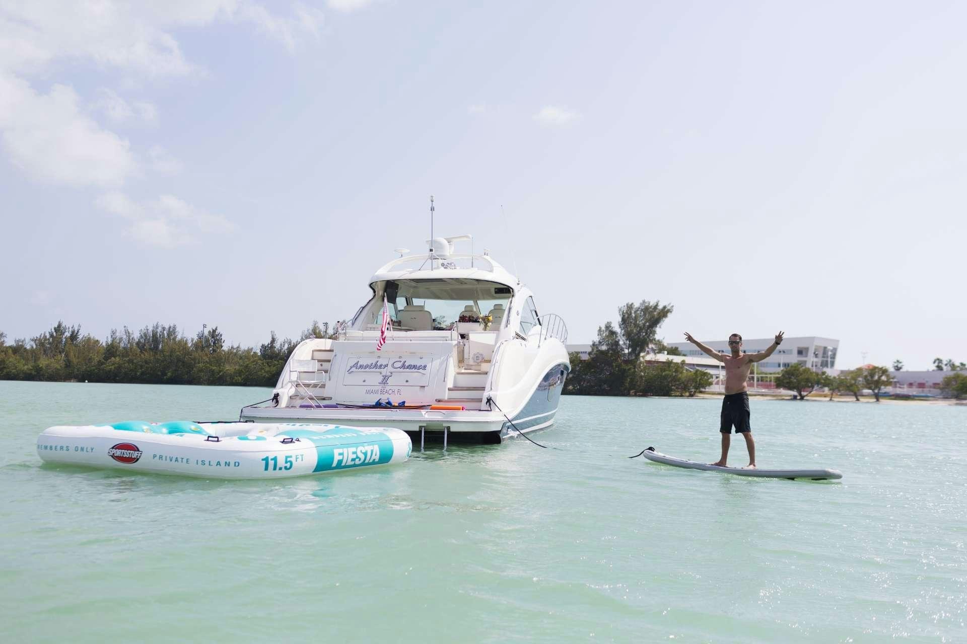 a person standing on a surfboard in the water next to a boat aboard ANOTHER CHANCE II Yacht for Charter