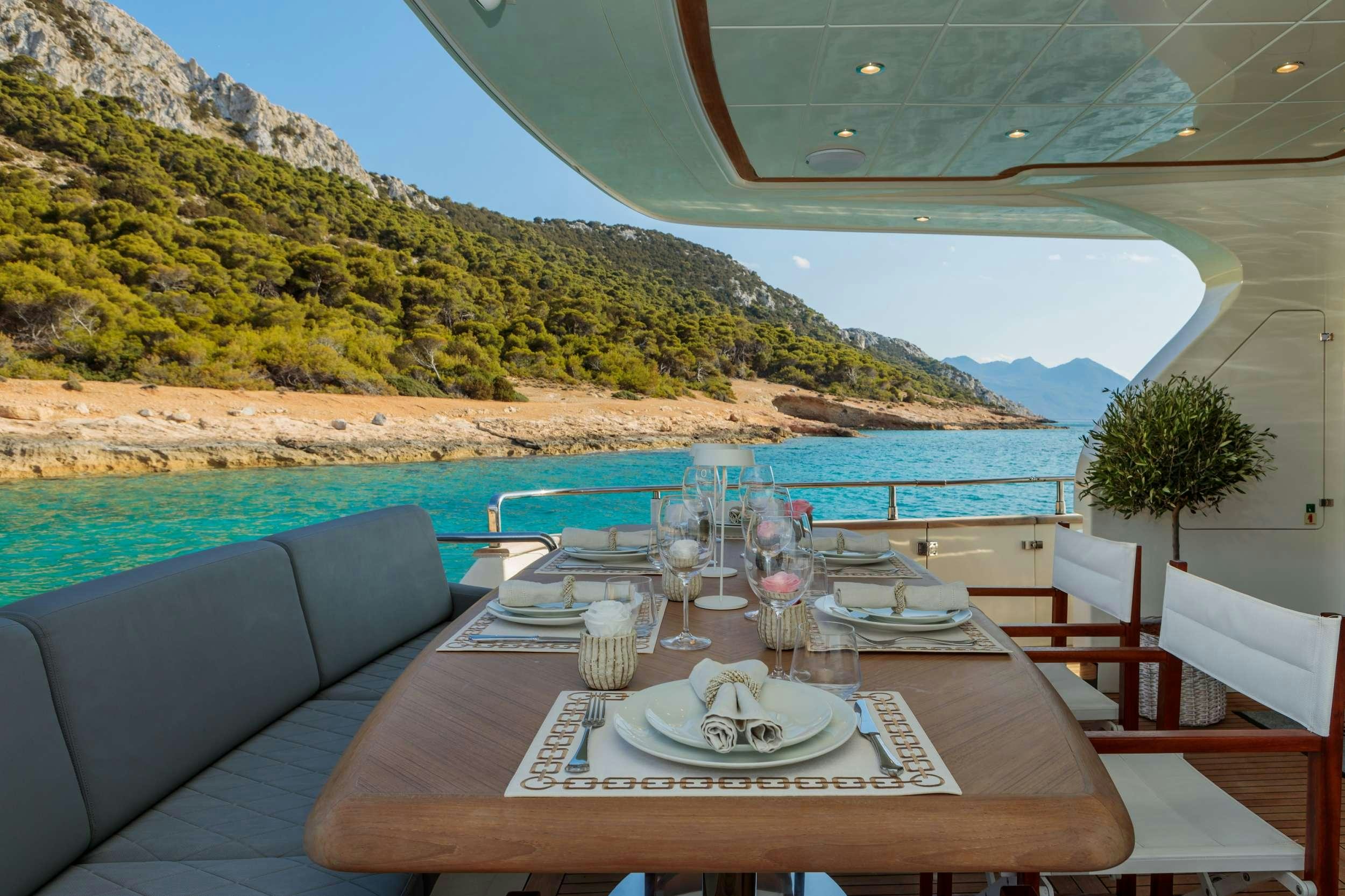 a table set for a meal on a balcony overlooking a large body of water aboard FREEDOM Yacht for Charter
