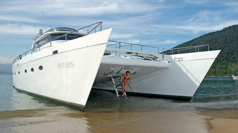 two people walking on a beach next to a white boat aboard ATLANTIS II Yacht for Charter