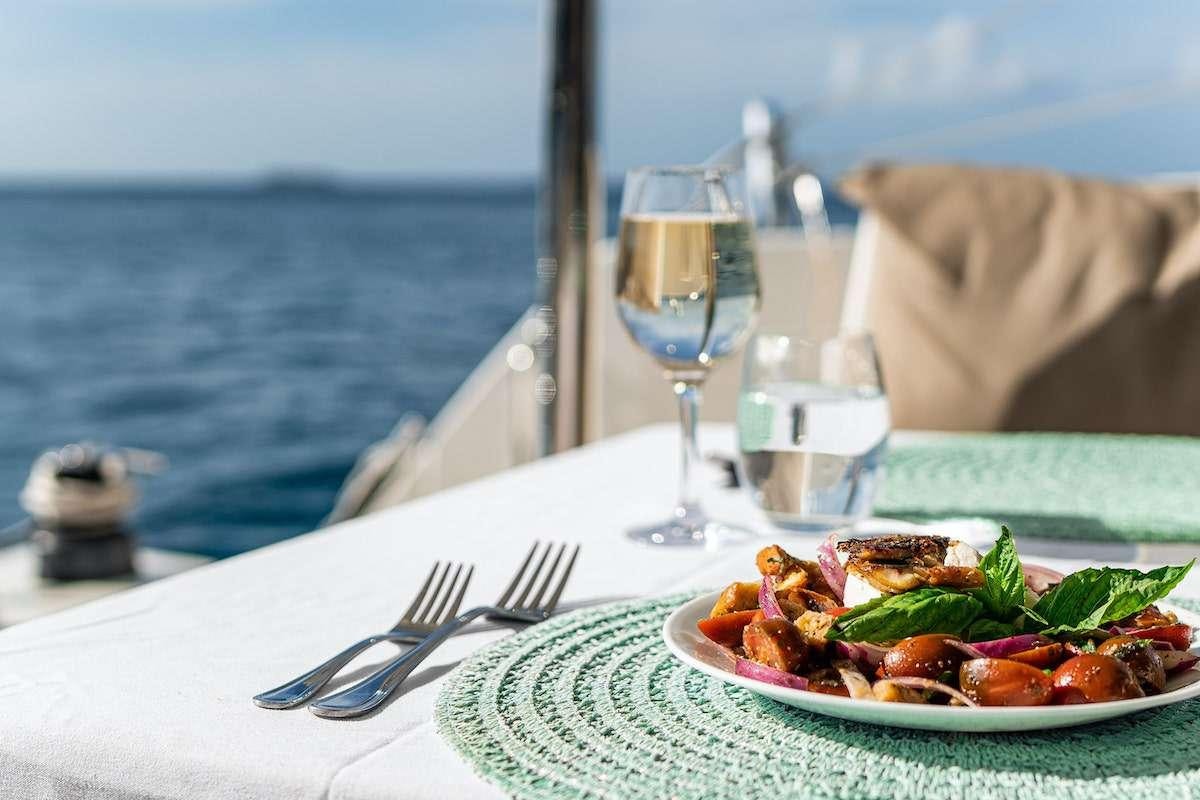 a plate of food and a glass of wine on a table aboard EDDIES IN TIME Yacht for Charter