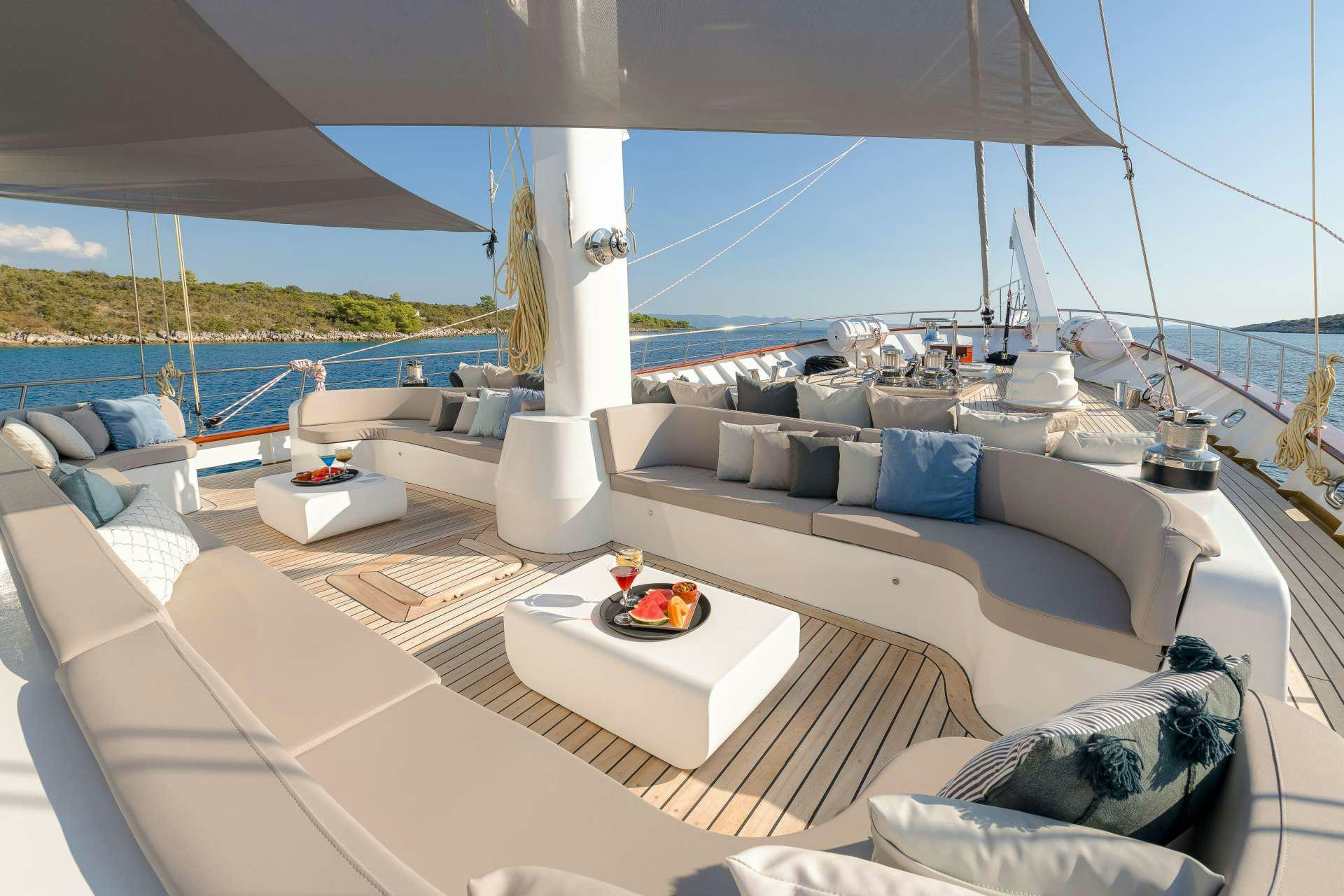 a large white lounge chair with a white sofa and a large white bed with a blue pillow on aboard LADY GITA Yacht for Charter