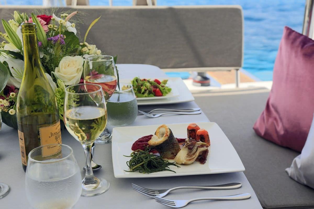 a table with plates of food and glasses of wine aboard DANIELA II Yacht for Charter
