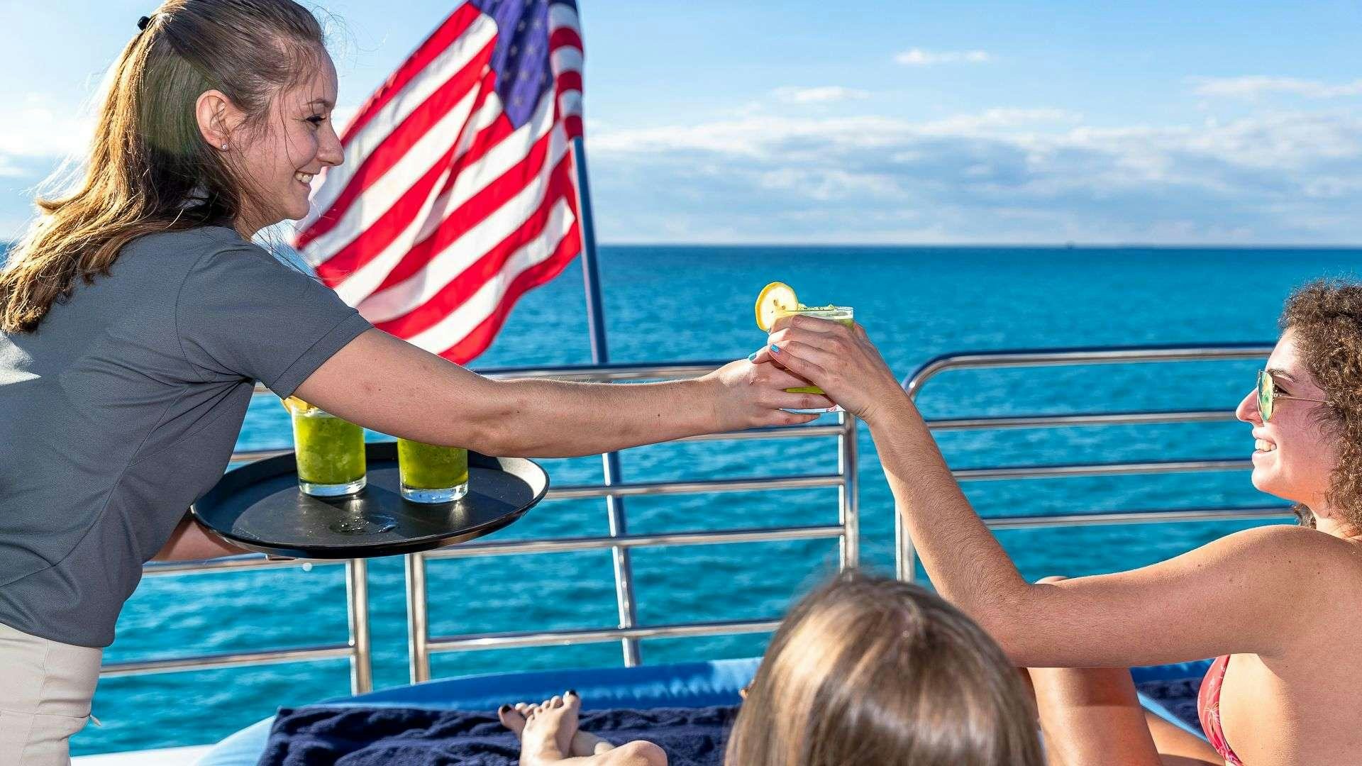 a woman and a man holding a drink and a flag aboard KEFI Yacht for Charter