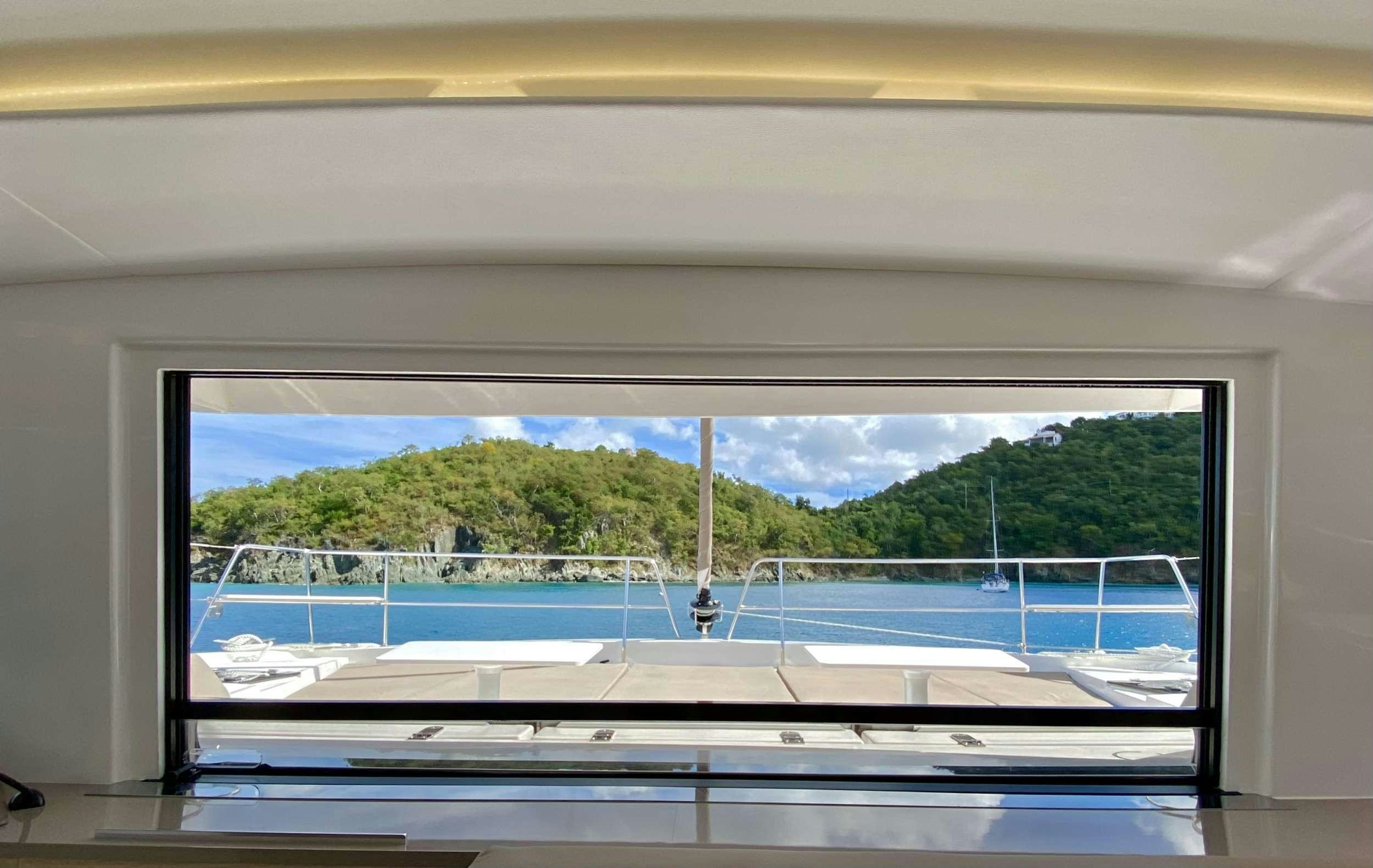 a window with a view of a beach and trees aboard FREESTYLE Yacht for Charter