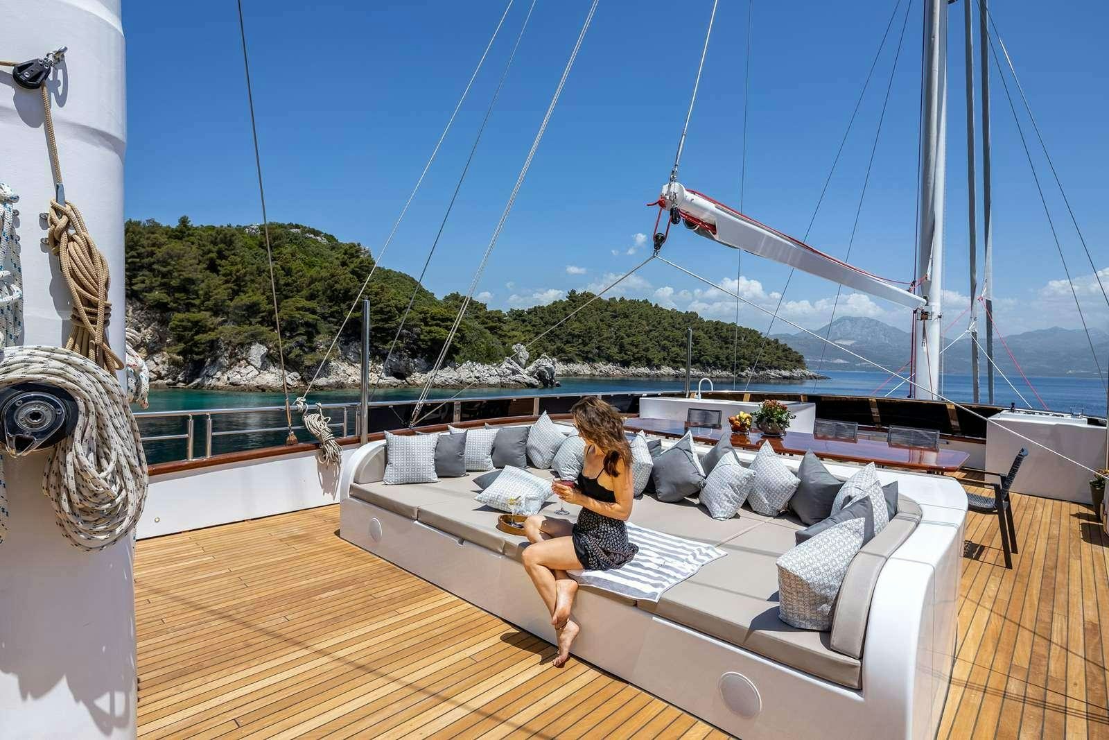 a person sitting on a couch on a deck with a large body of water and trees in the aboard LOVE STORY Yacht for Charter