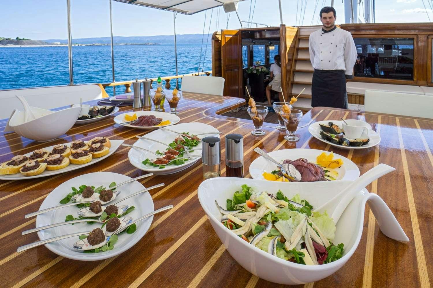 a table with plates of food and a person standing behind it aboard STELLA MARIS Yacht for Charter