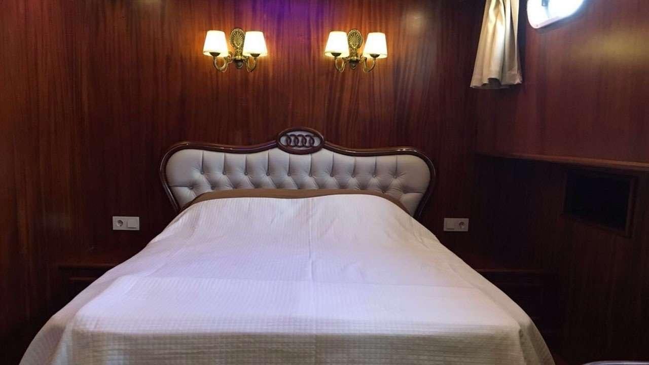 a bed with a white sheet and a headboard with a red wall aboard M/S E.ARDA DENIZ Yacht for Charter