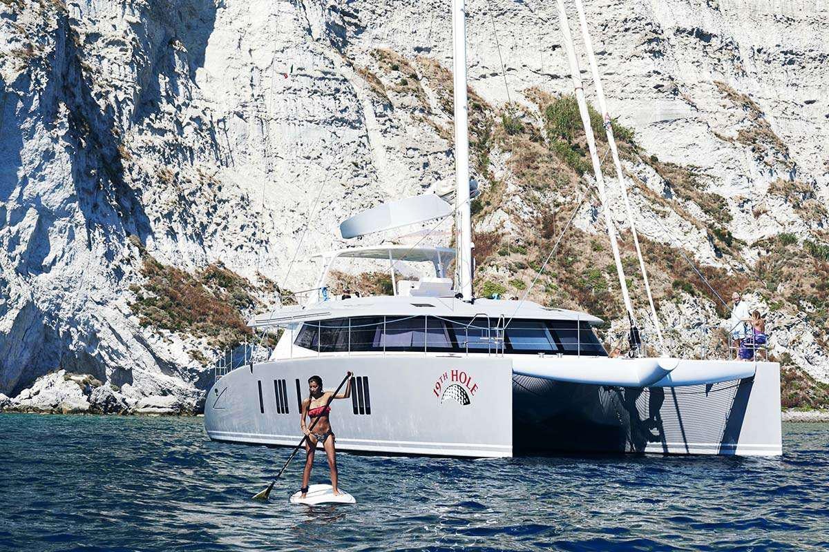 a man on a surfboard in the water next to a boat aboard 19TH HOLE Yacht for Charter