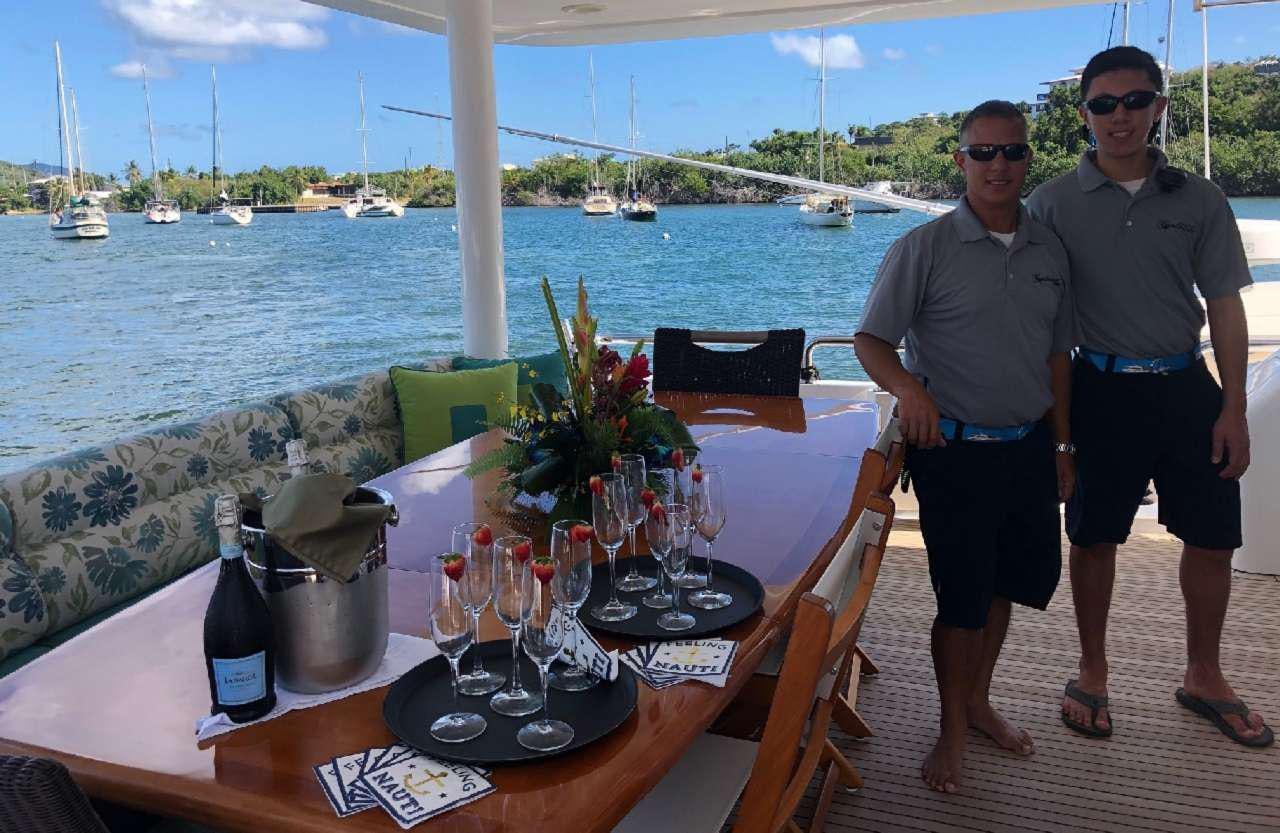 a couple of men standing by a table with wine glasses and a bottle of wine on it aboard CYNDERELLA Yacht for Charter