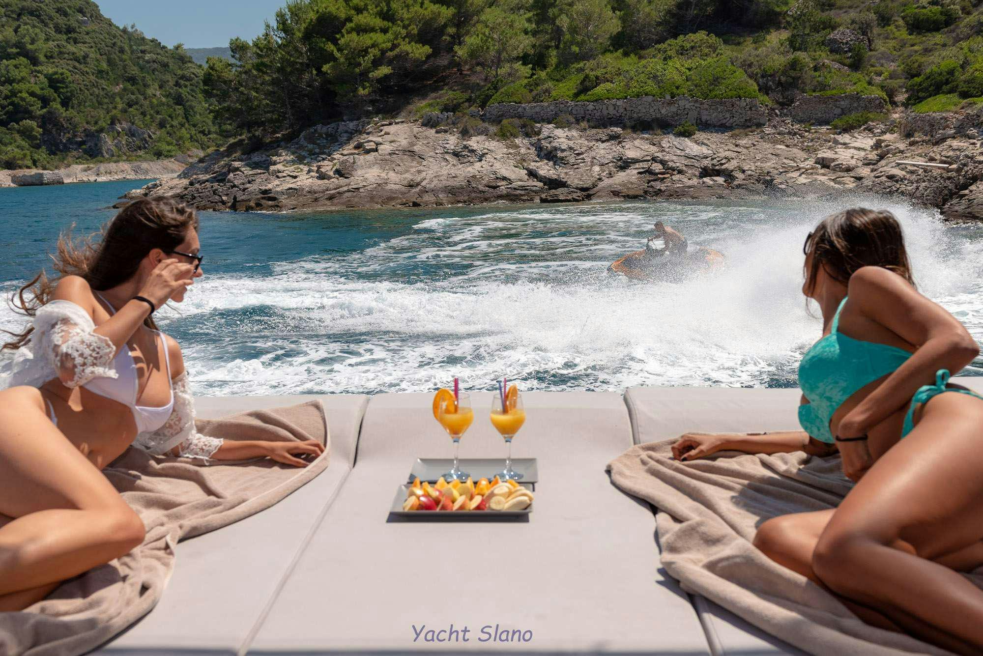a group of people sitting on a beach with a table of food and drinks aboard SLANO Yacht for Charter