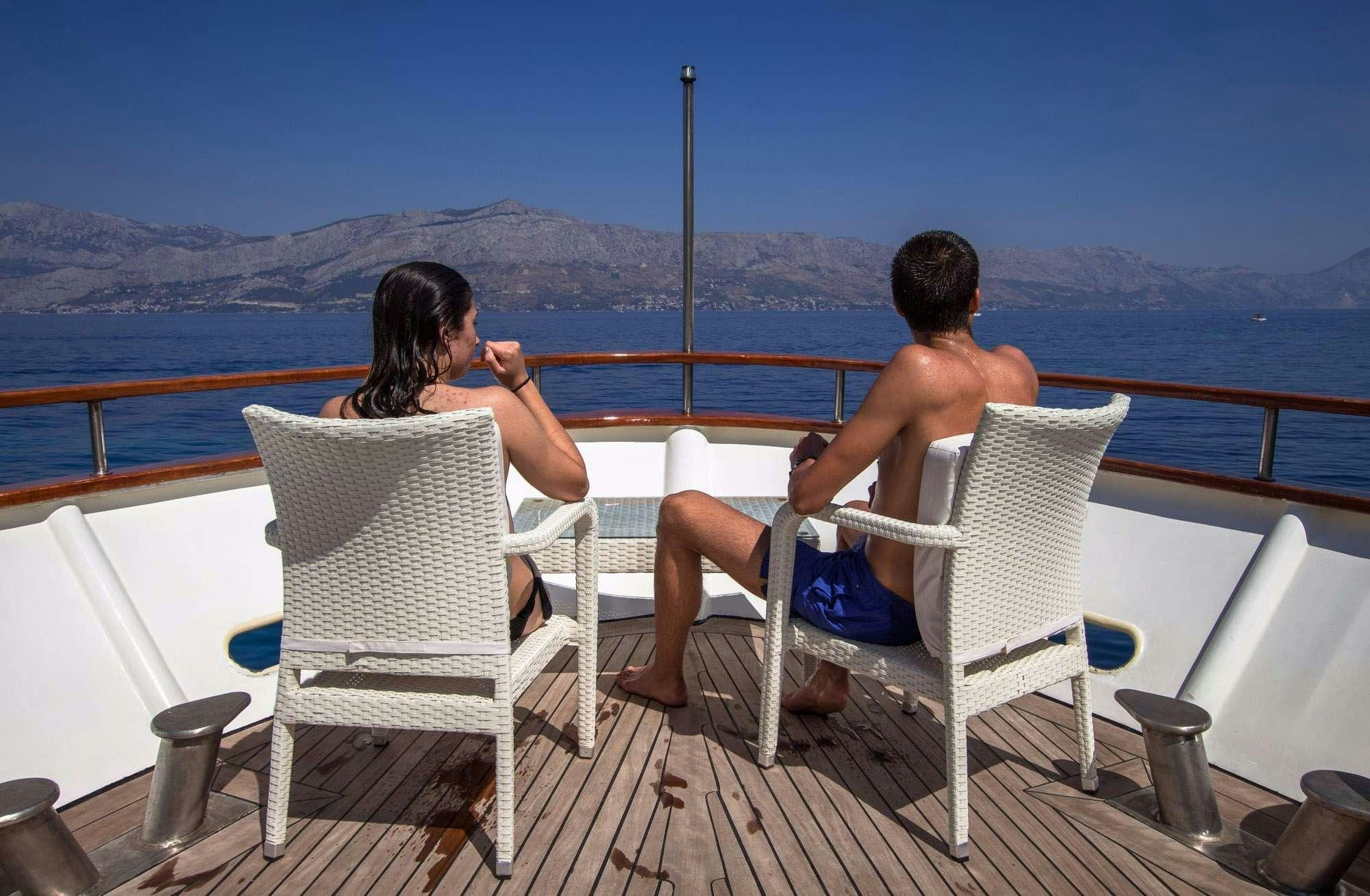 a couple of people sitting on chairs on a deck overlooking a large body of water aboard KORAB Yacht for Charter