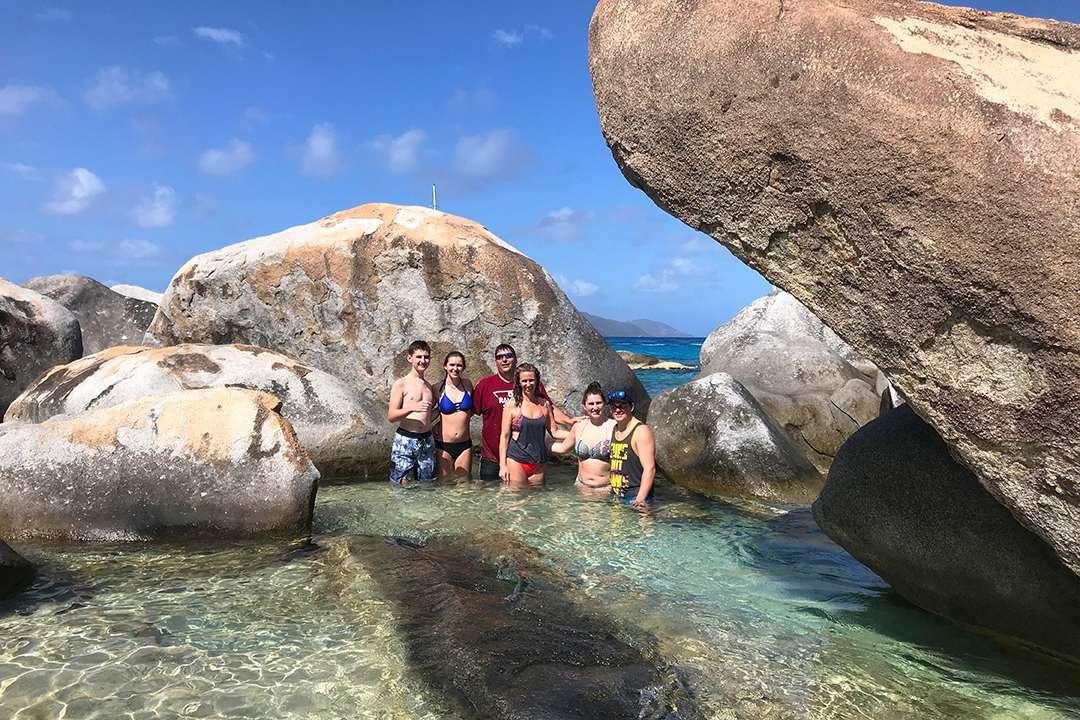 a group of people standing in water by rocks and a rock aboard QUEST Yacht for Charter