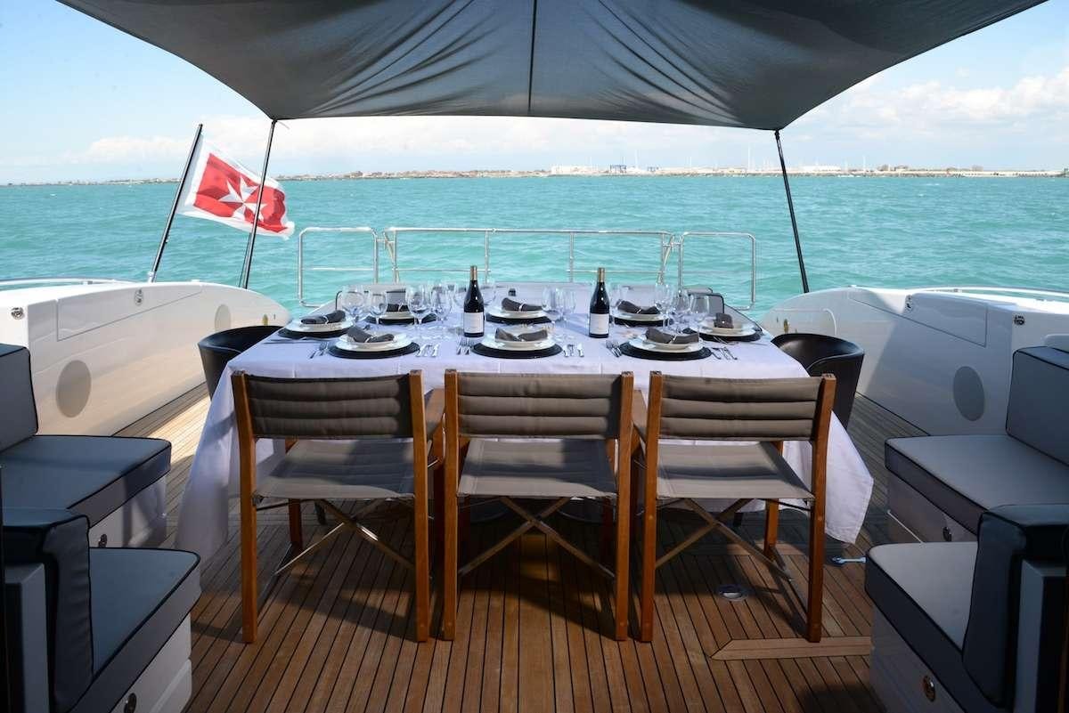 a table set with chairs and a flag on a deck with a body of water in the background aboard ONLY ONE Yacht for Charter