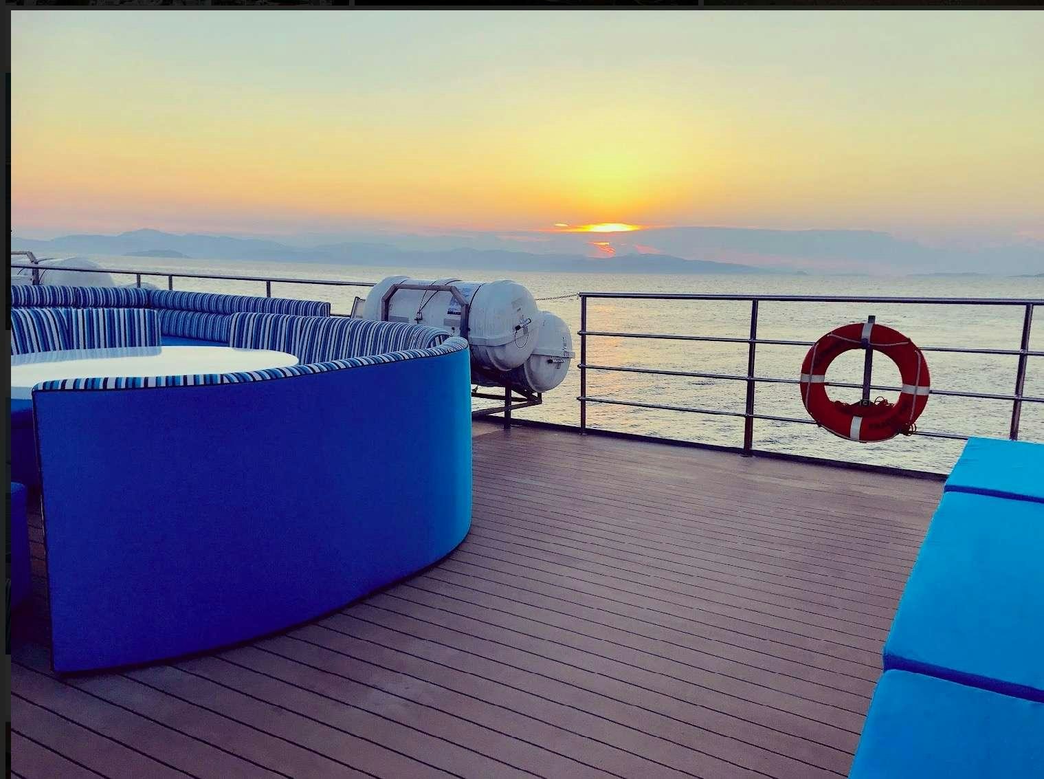 a deck with a view of the ocean and the sun setting aboard HARMONY Yacht for Charter