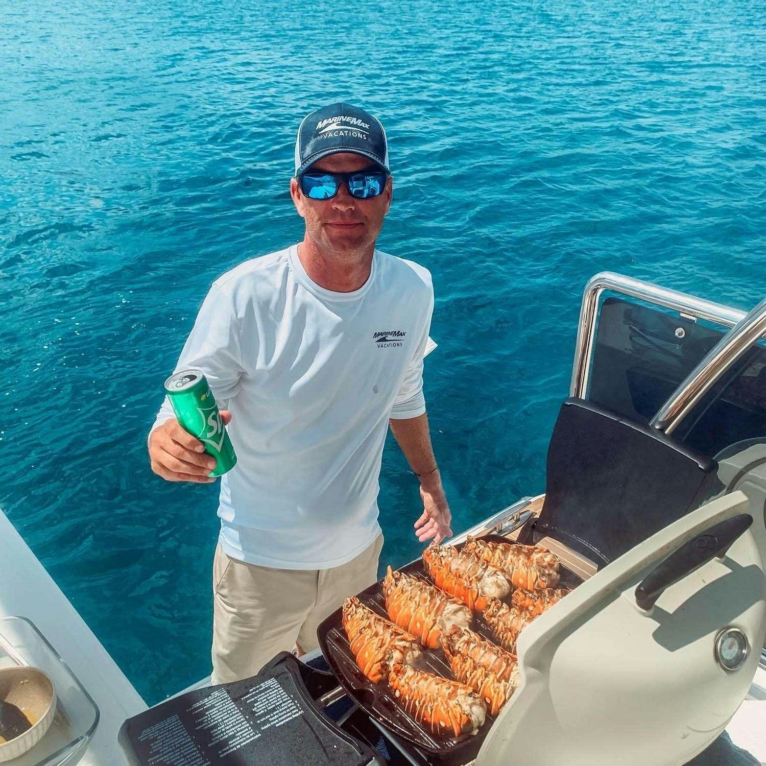 a man in a white shirt and sunglasses standing on a boat with a tray of food aboard GO TEAM Yacht for Charter