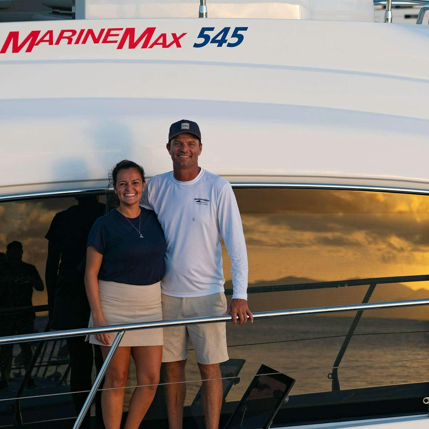 a man and woman standing on a balcony with a sunset behind them aboard GO TEAM Yacht for Charter