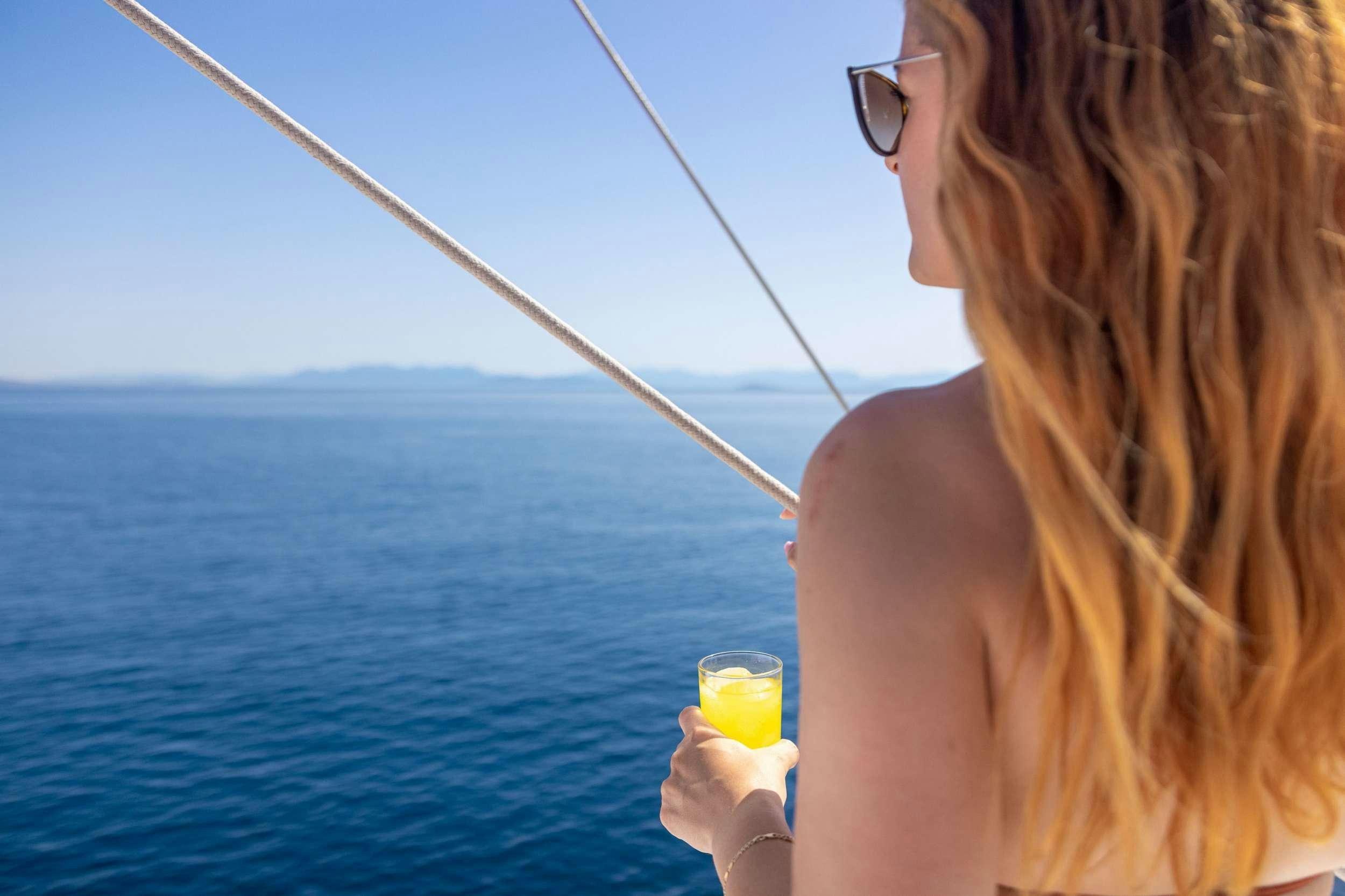 a woman holding a drink and looking out at the ocean aboard MELTEMI Yacht for Charter