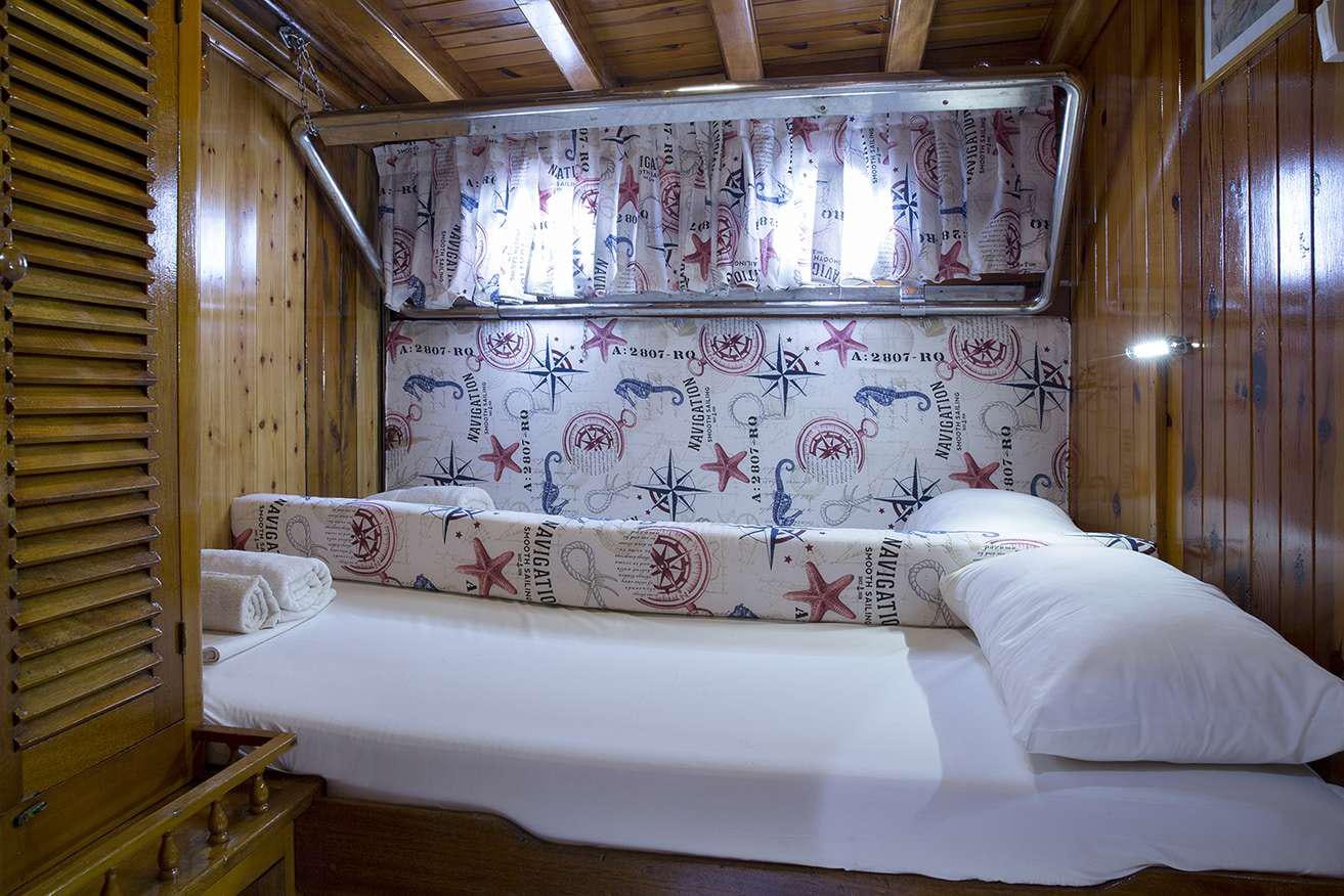 a bed with a white sheet and a window with floral designs aboard MELTEMI Yacht for Charter