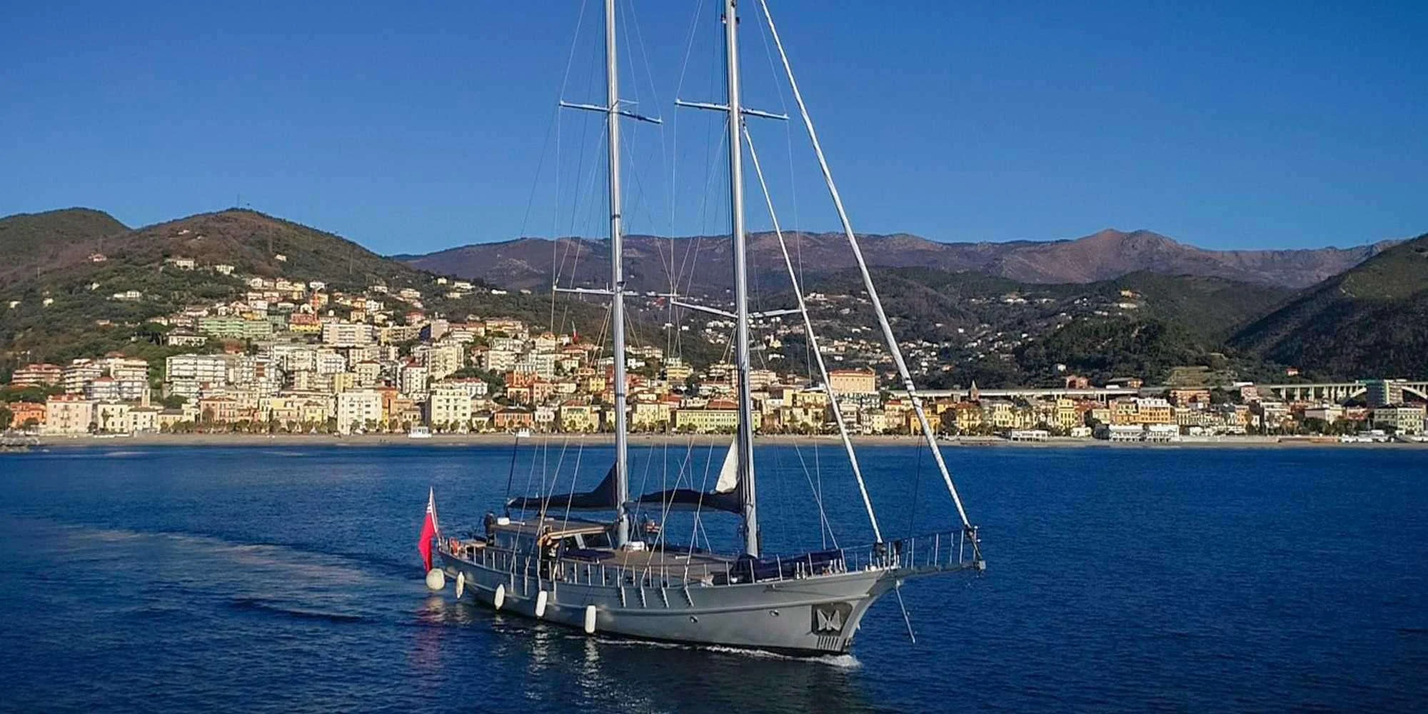 A stunning yacht sails gracefully along the coastline with a picturesque town in the background. aboard LA MER Yacht for Charter
