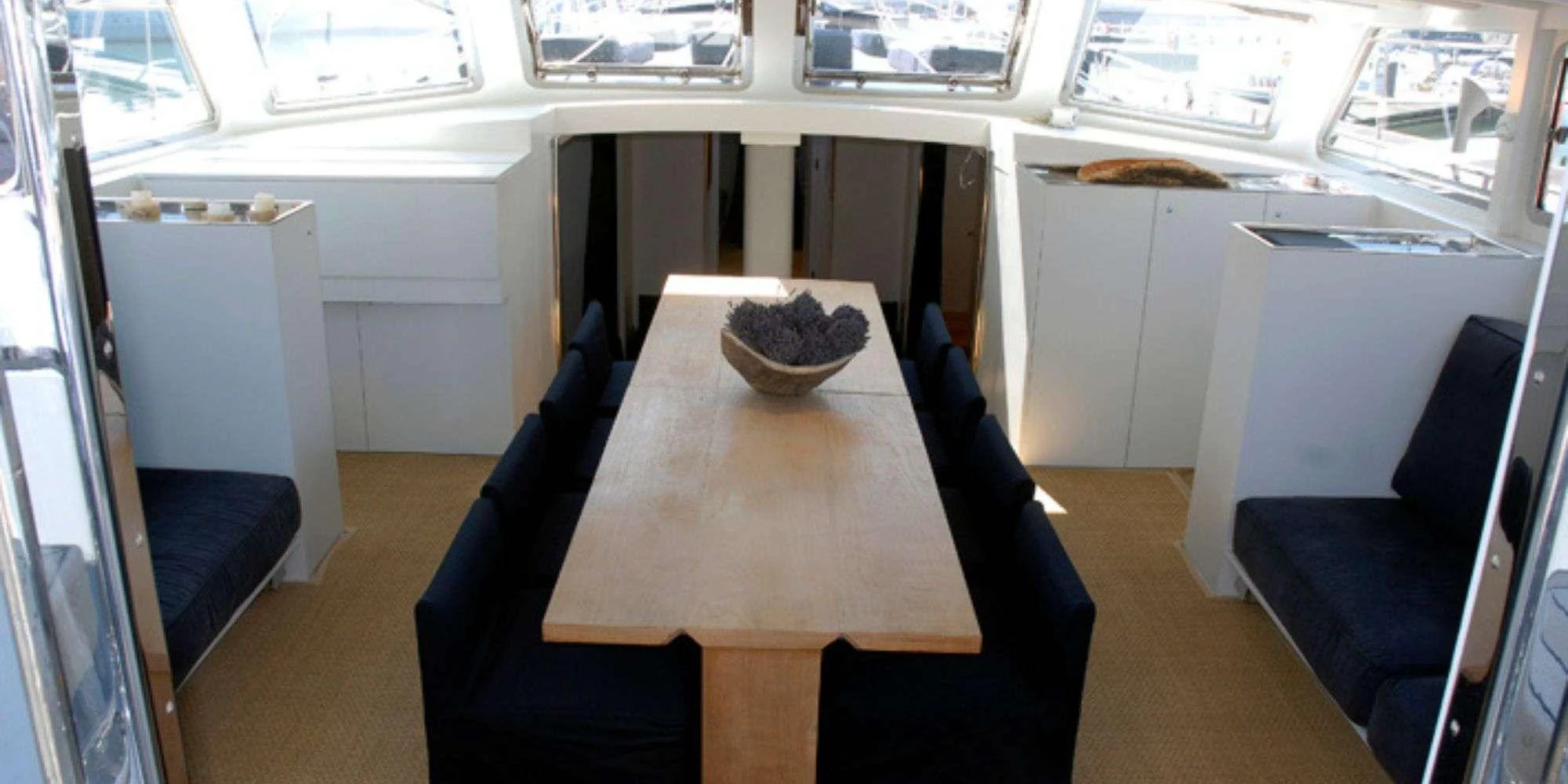 The yacht's dining area features a sleek wooden table surrounded by comfortable seating, bathed in natural light from large windows. aboard LA MER Yacht for Charter