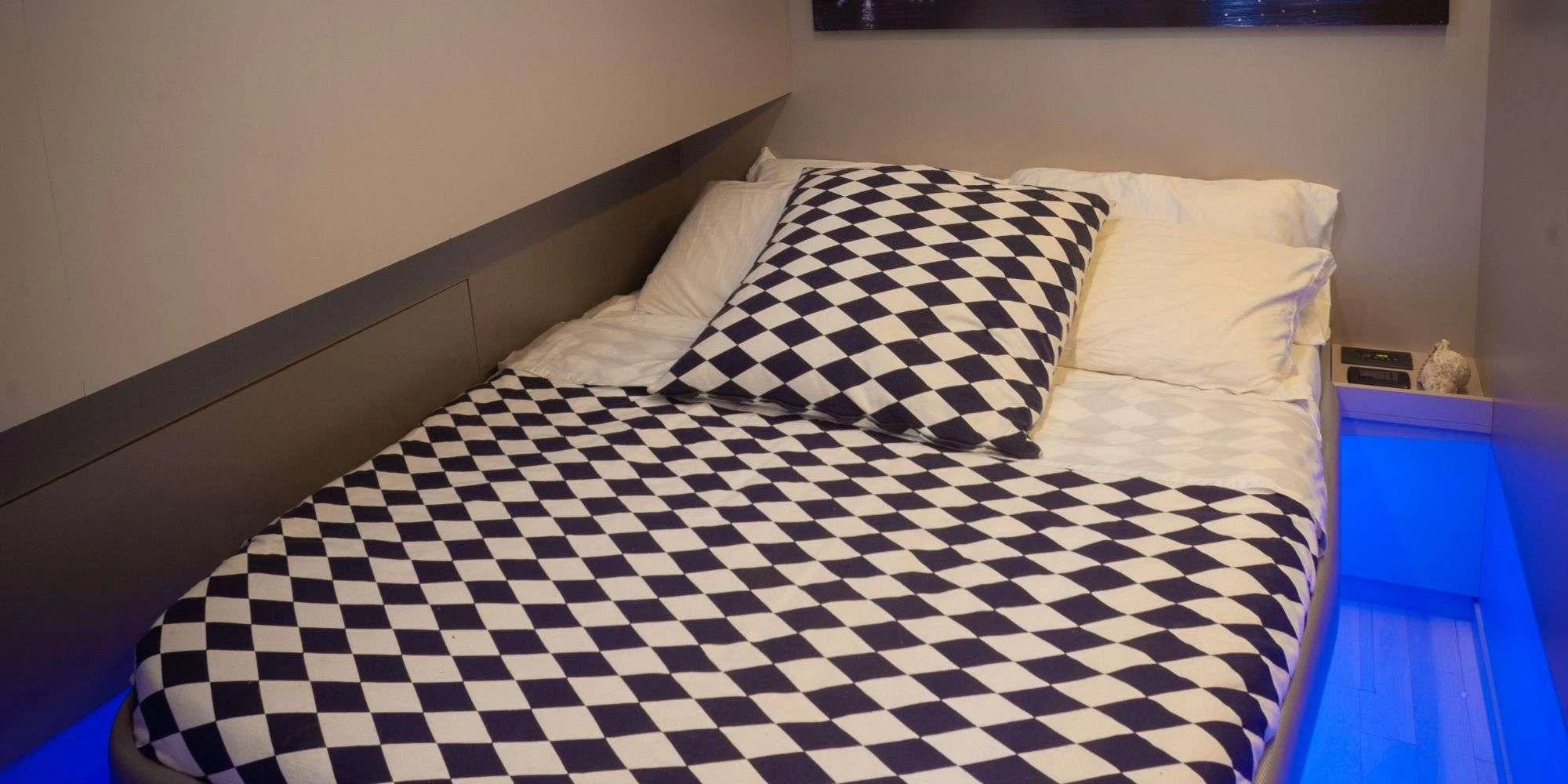 A cozy stateroom featuring a bed with a checkered duvet and ambient blue lighting. aboard LA MER Yacht for Charter