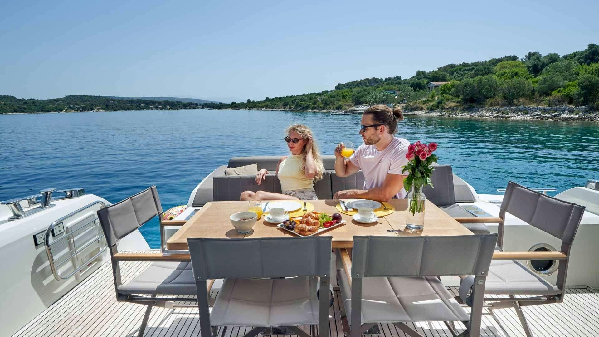a couple sitting at a table on a boat with a drink and flowers aboard SIMULL Yacht for Charter