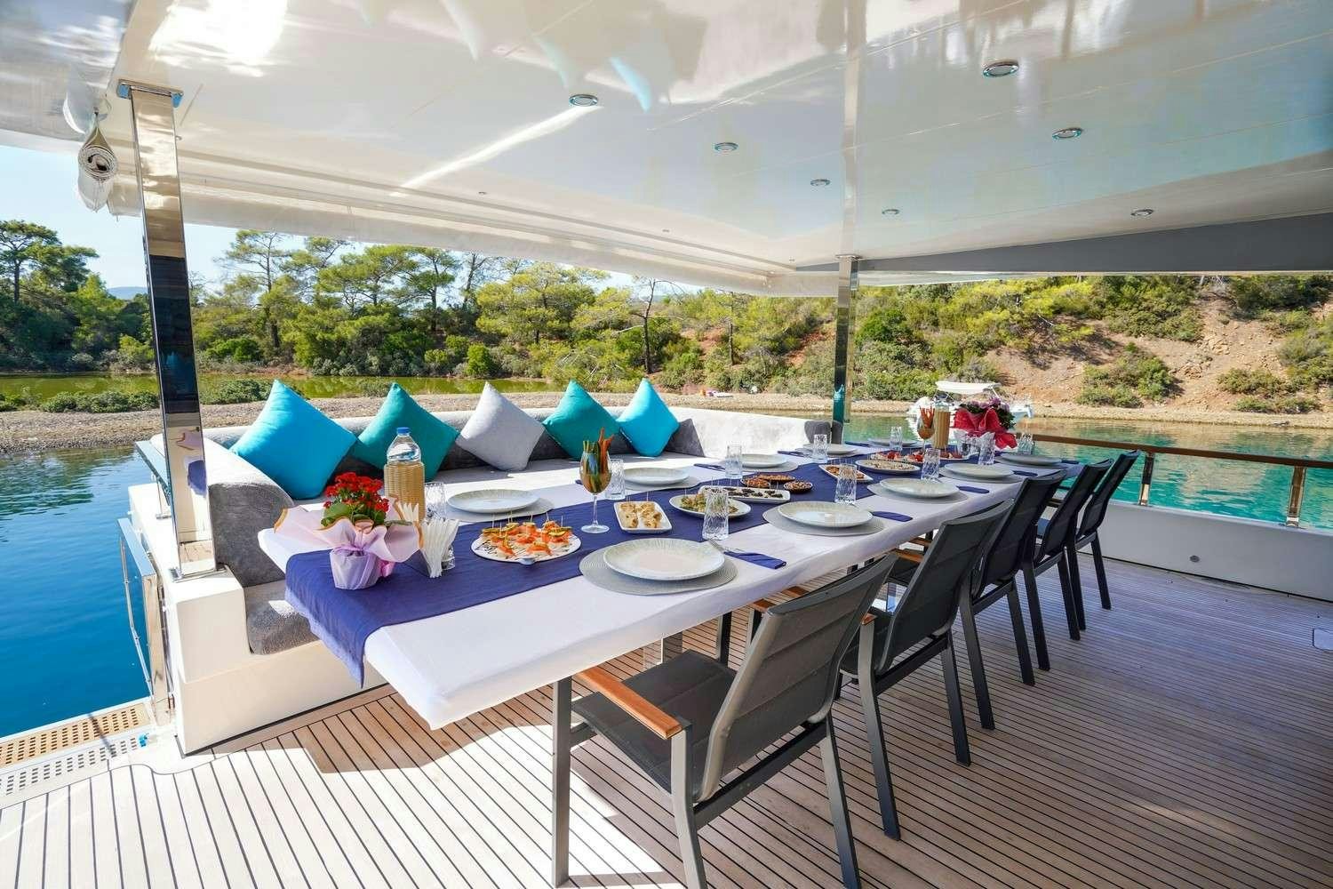 a table set for a meal on a deck with a view of the water and trees aboard CINAR YILDIZI Yacht for Charter