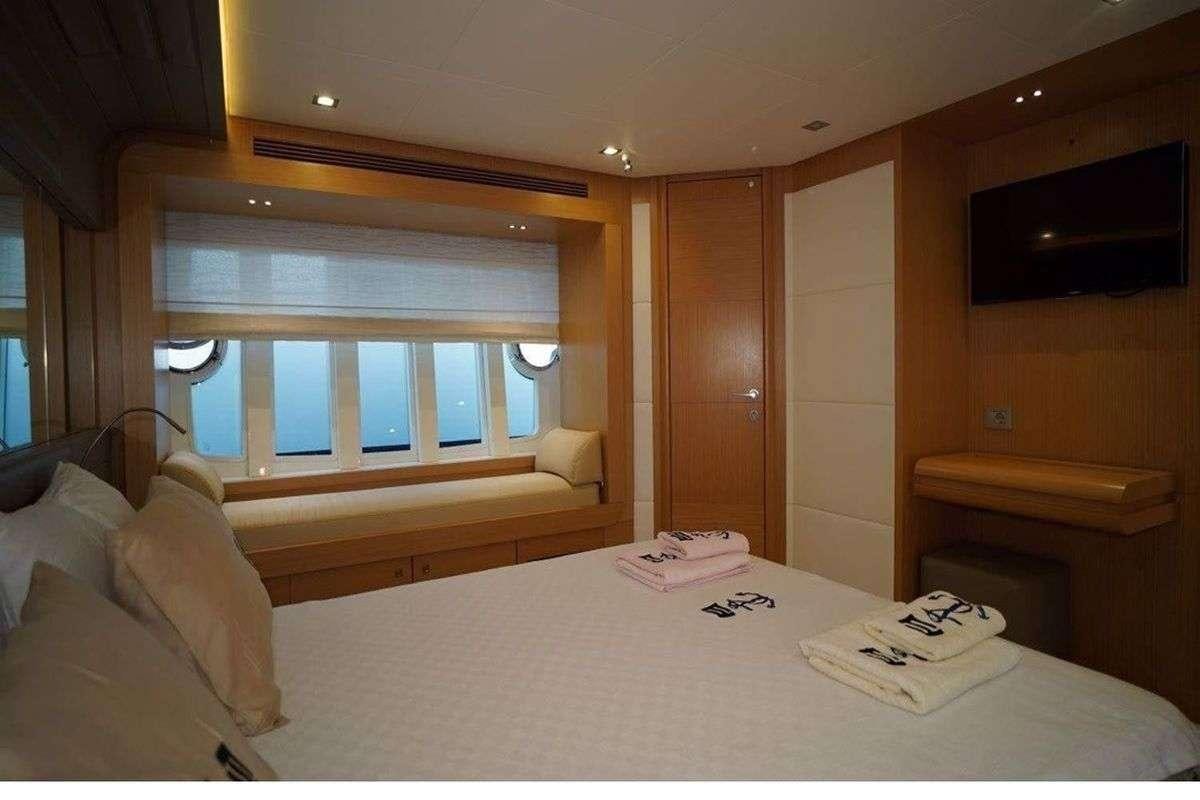 a bed with a white sheet and a window with a view of the city aboard REINE DES COEURS Yacht for Charter