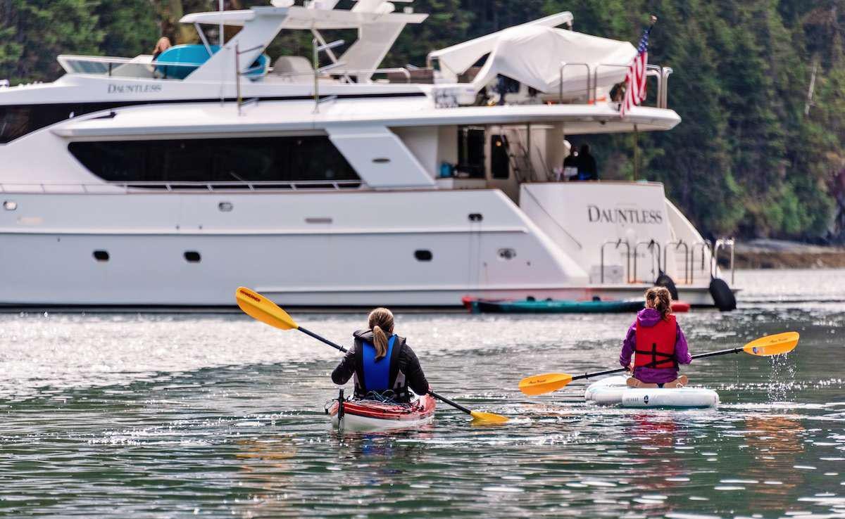 a couple of people on paddle boards in front of a boat aboard DAUNTLESS Yacht for Charter