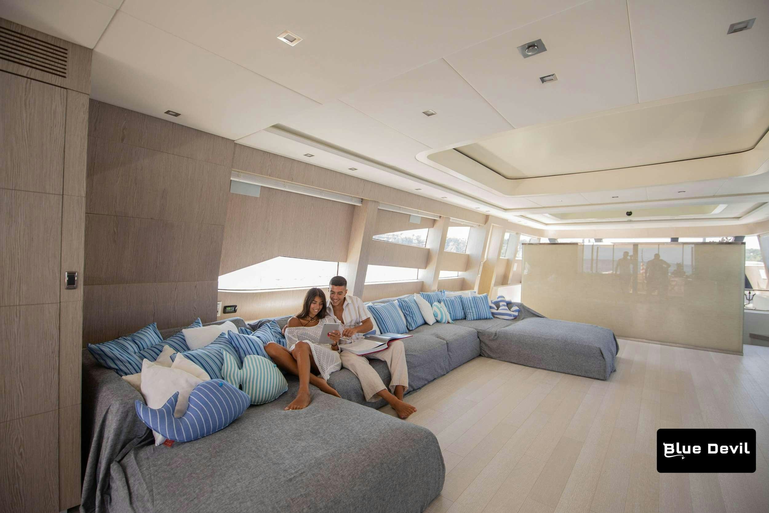 a couple of people sitting on a couch in a room with a wood door and a white ceiling aboard BLUE DEVIL Yacht for Charter