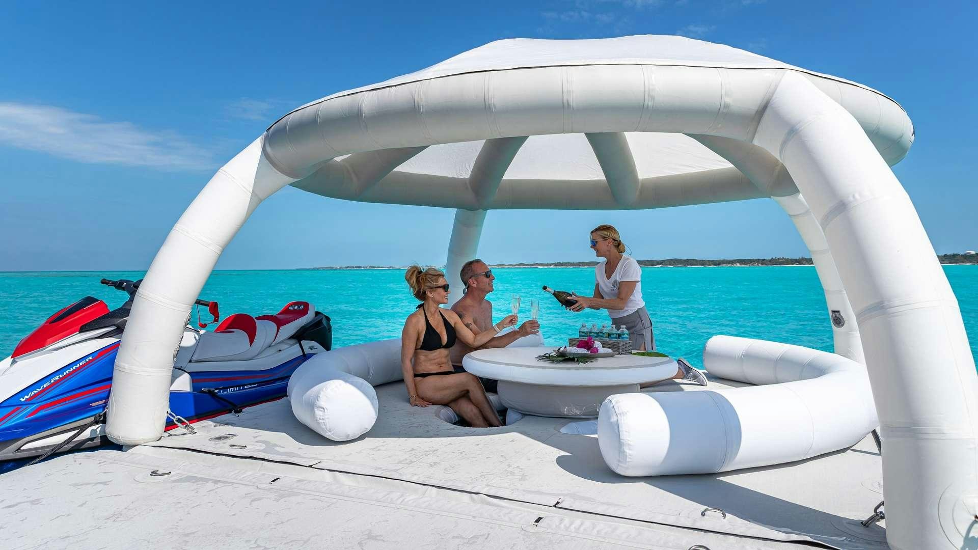 a group of people sitting on a beach with a white tent and water aboard WHITE PEARL Yacht for Charter