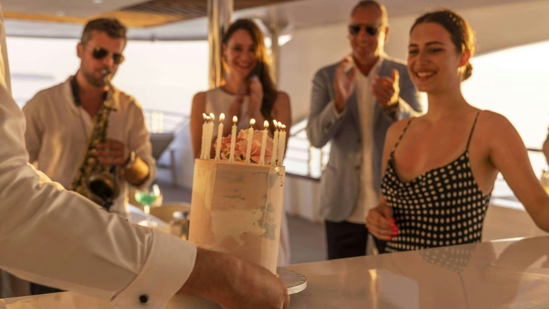 a group of people standing around a table with a cake and a bottle of champagne aboard M/Y ANTHEA Yacht for Charter