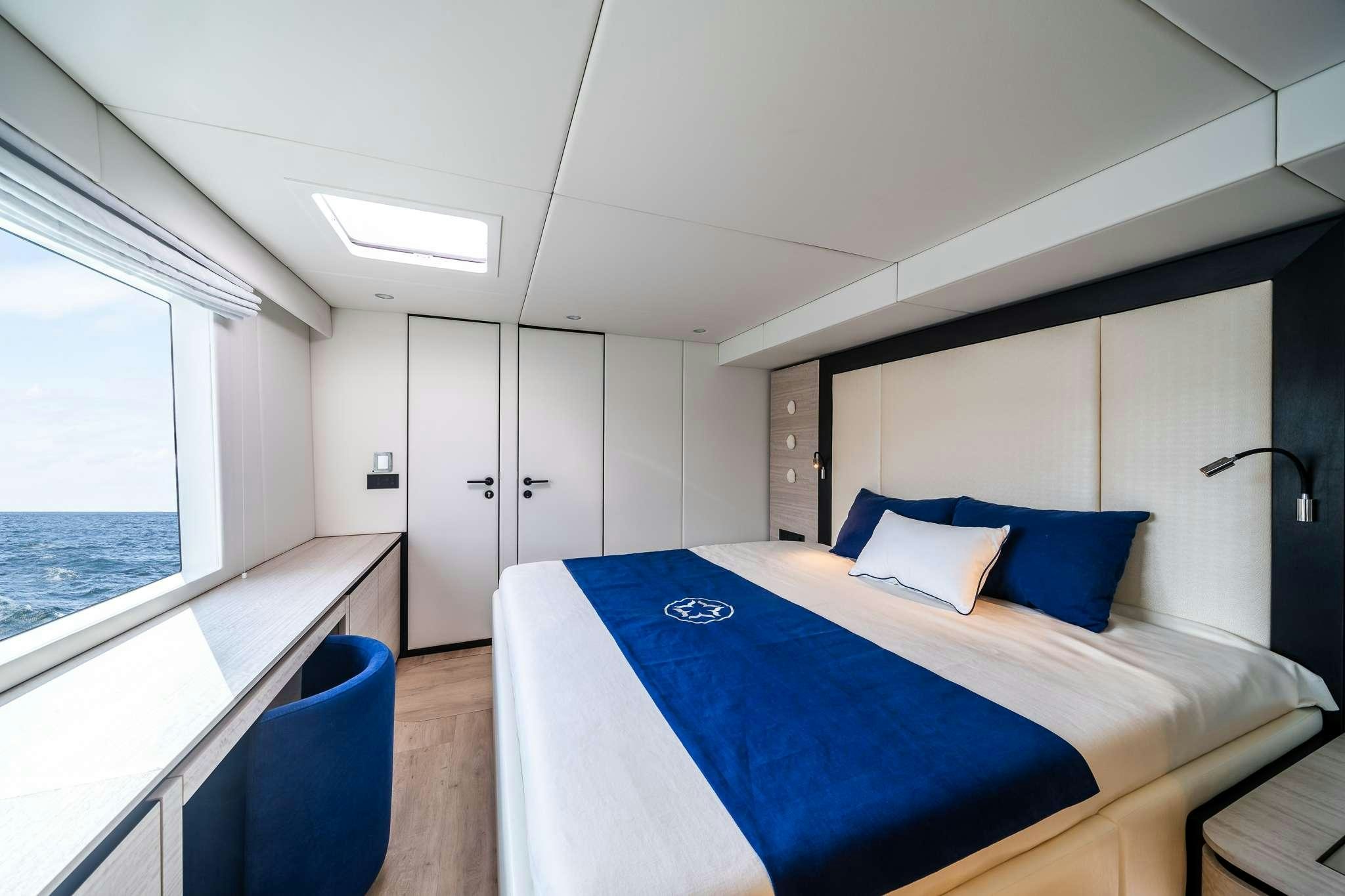 a room with a bed and a blue table and a window aboard ONE PLANET Yacht for Charter
