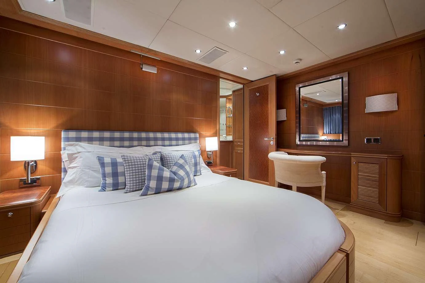 The stateroom features a plush bed with checkered pillows, warm wood paneling, and elegant lighting. aboard MAC BREW Yacht for Charter