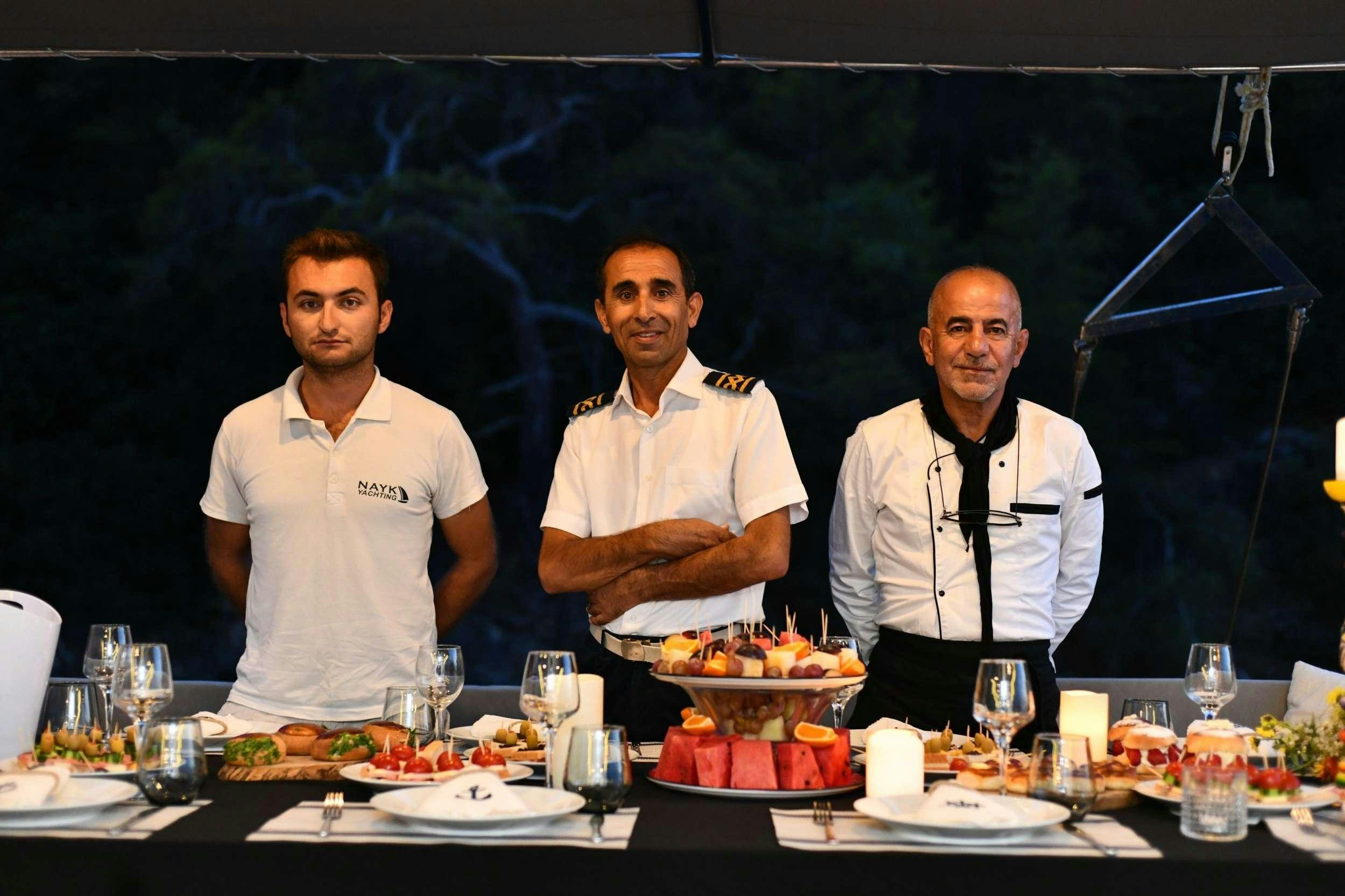 a group of men standing next to each other at a table with food aboard NAYK 2 Yacht for Charter