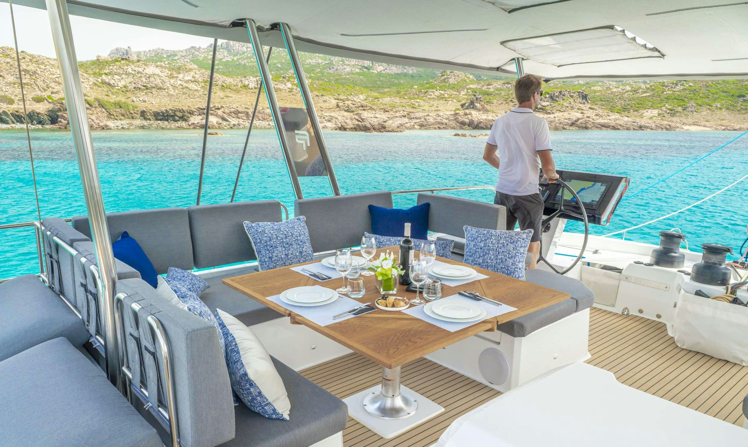a person standing on a deck of a boat with a table and chairs aboard SEMPER FIDELIS Yacht for Charter