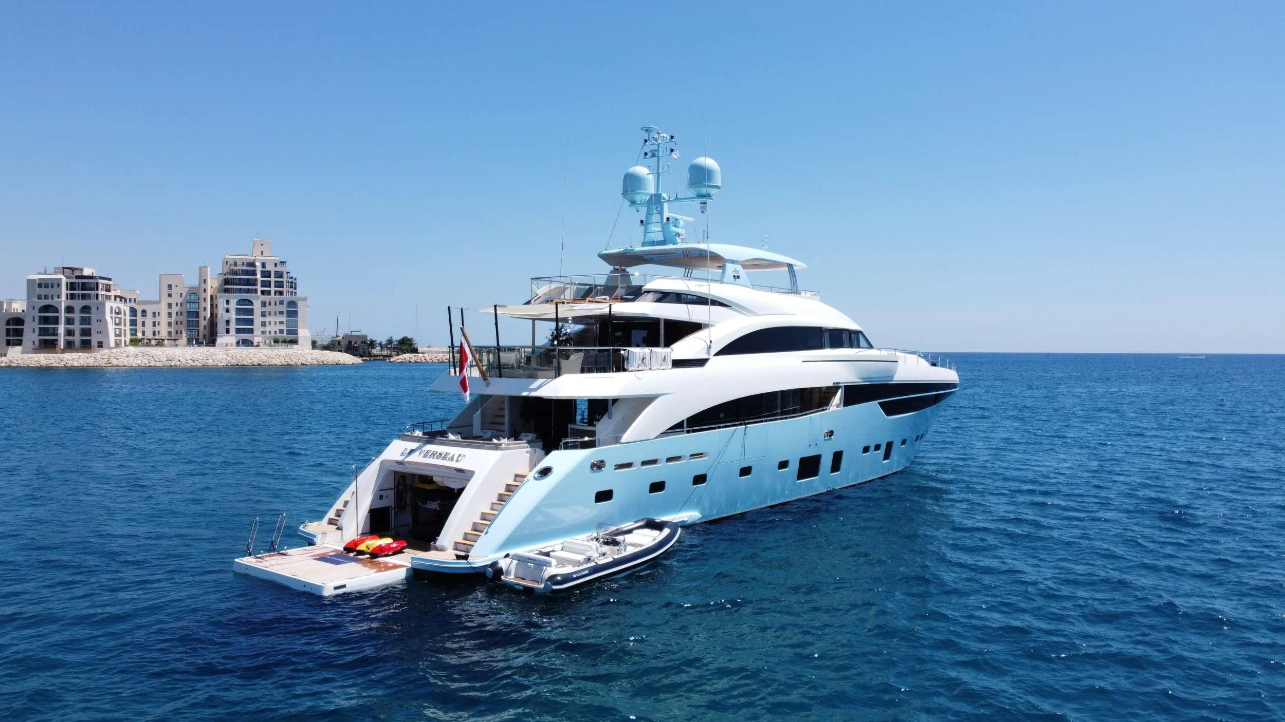 A luxurious yacht anchored in calm blue waters with a tender and water toys at the stern. aboard LE VERSEAU Yacht for Charter