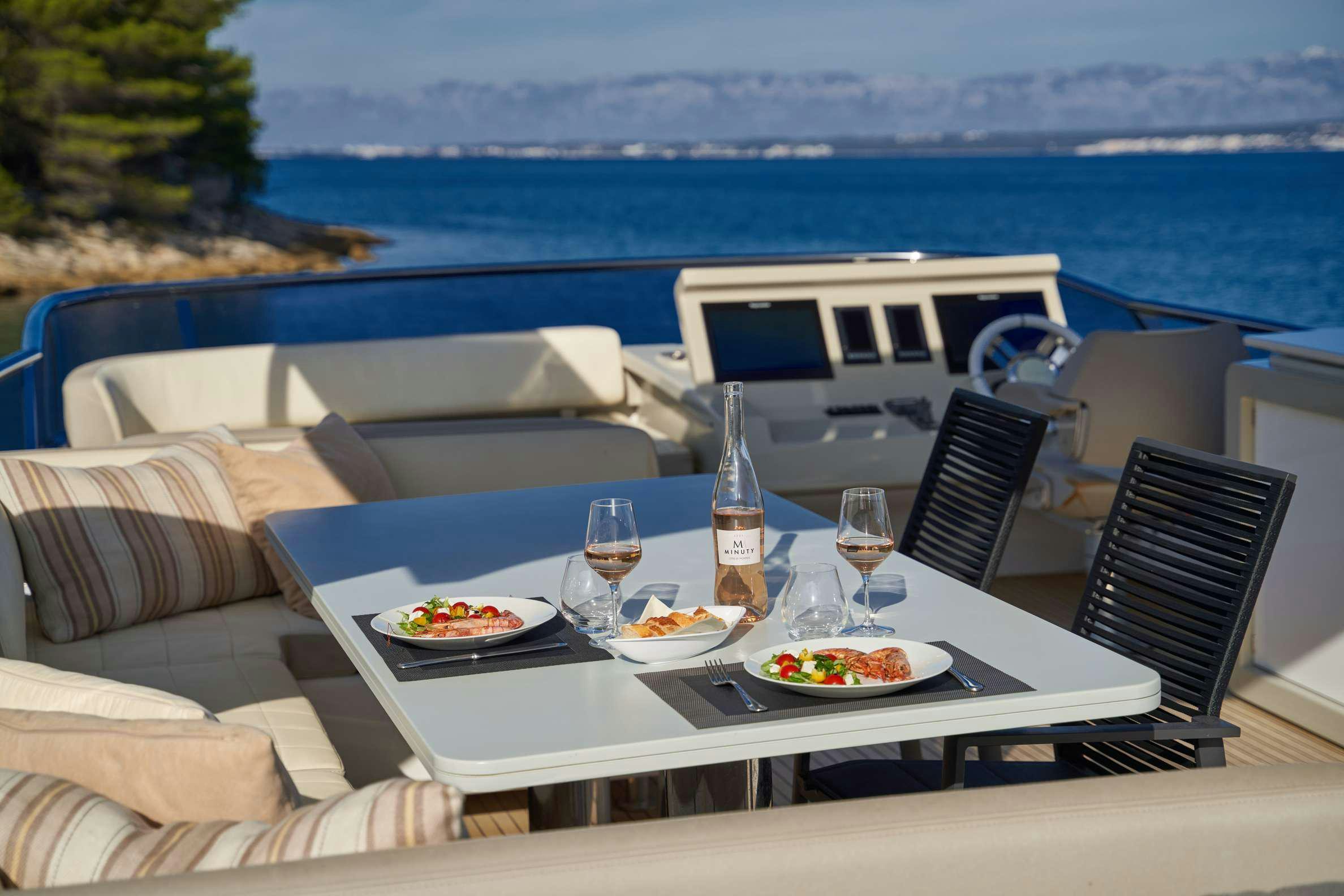 a table with food and wine on it by a body of water aboard AZIMUT 72 - RELAX OF Yacht for Charter