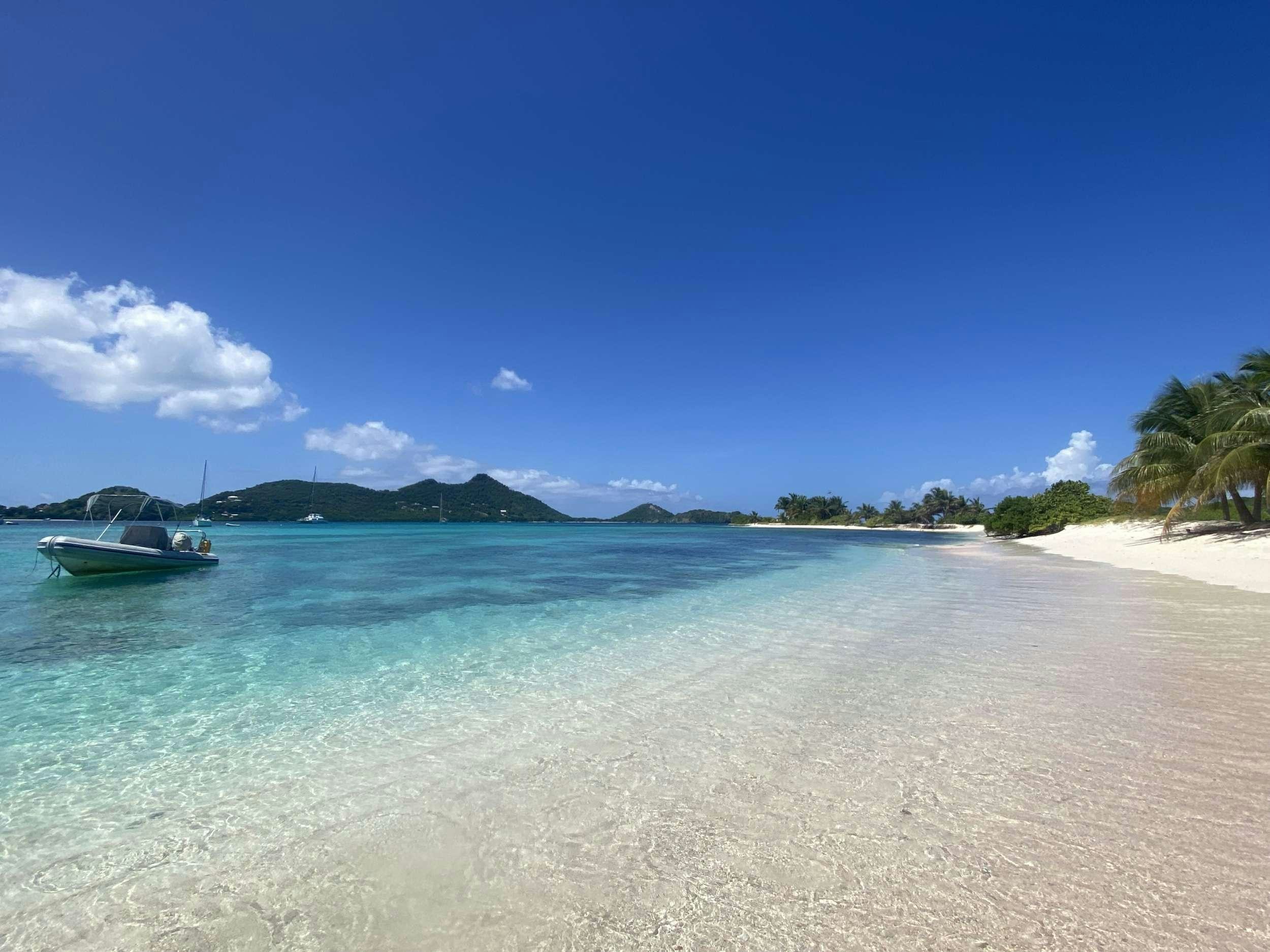 a beach with a boat and a beach and mountains in the background aboard HQ2 Yacht for Charter
