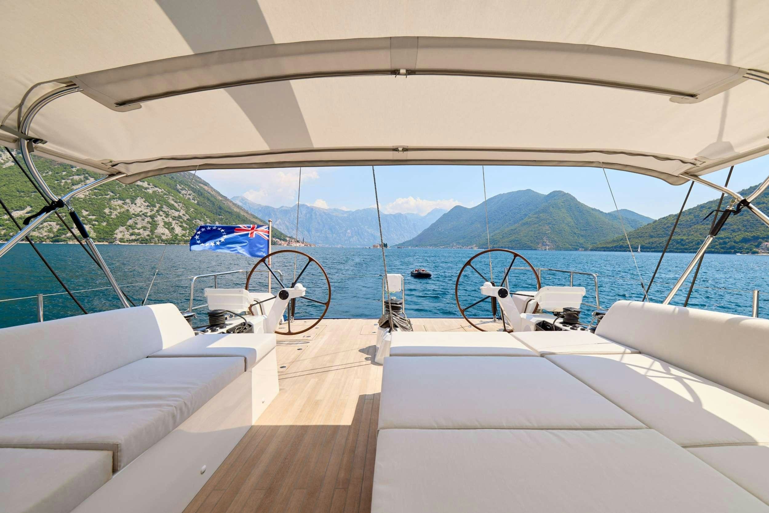 a boat with white beds and white pillows on a deck with a view of mountains and water aboard GRATEFUL Yacht for Charter