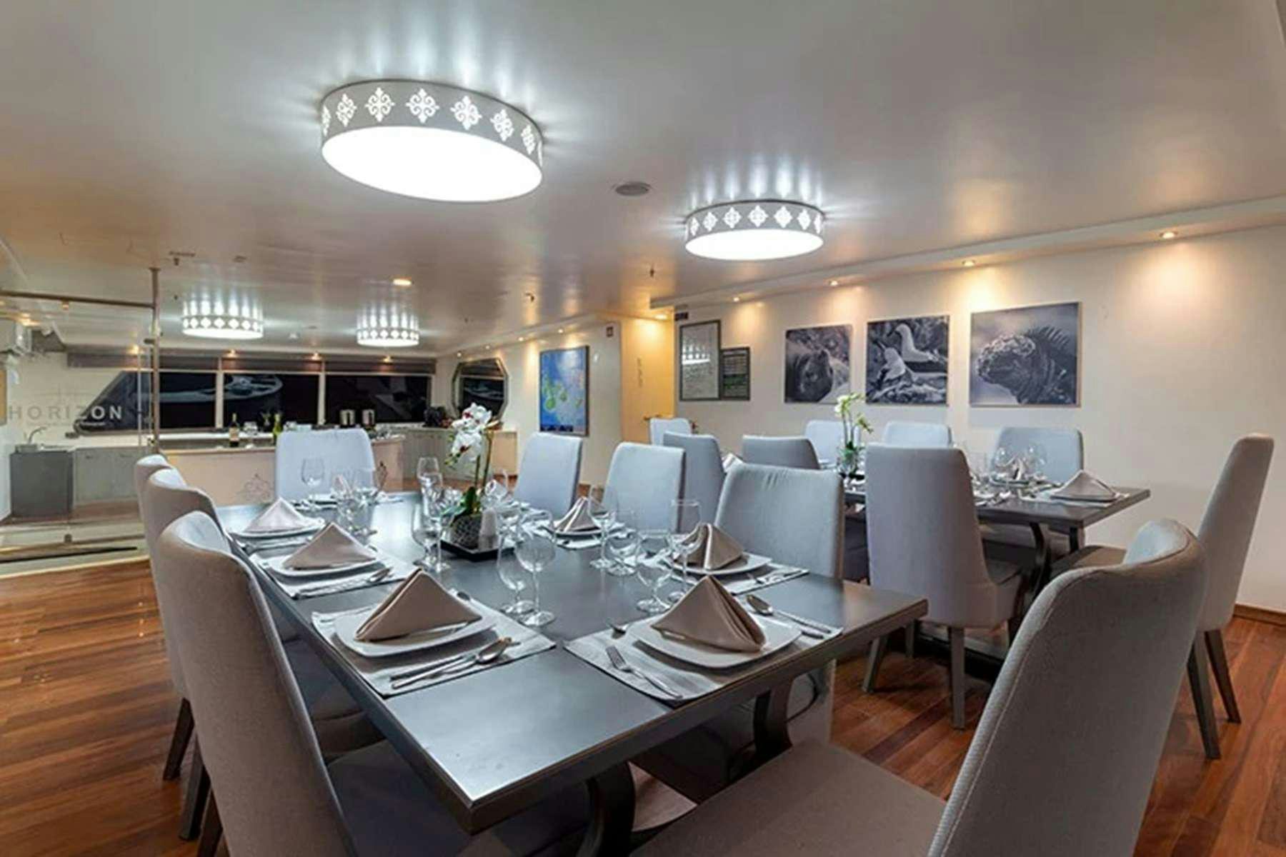 a large dining room with white chairs aboard GALAPAGOS HORIZON Yacht for Charter