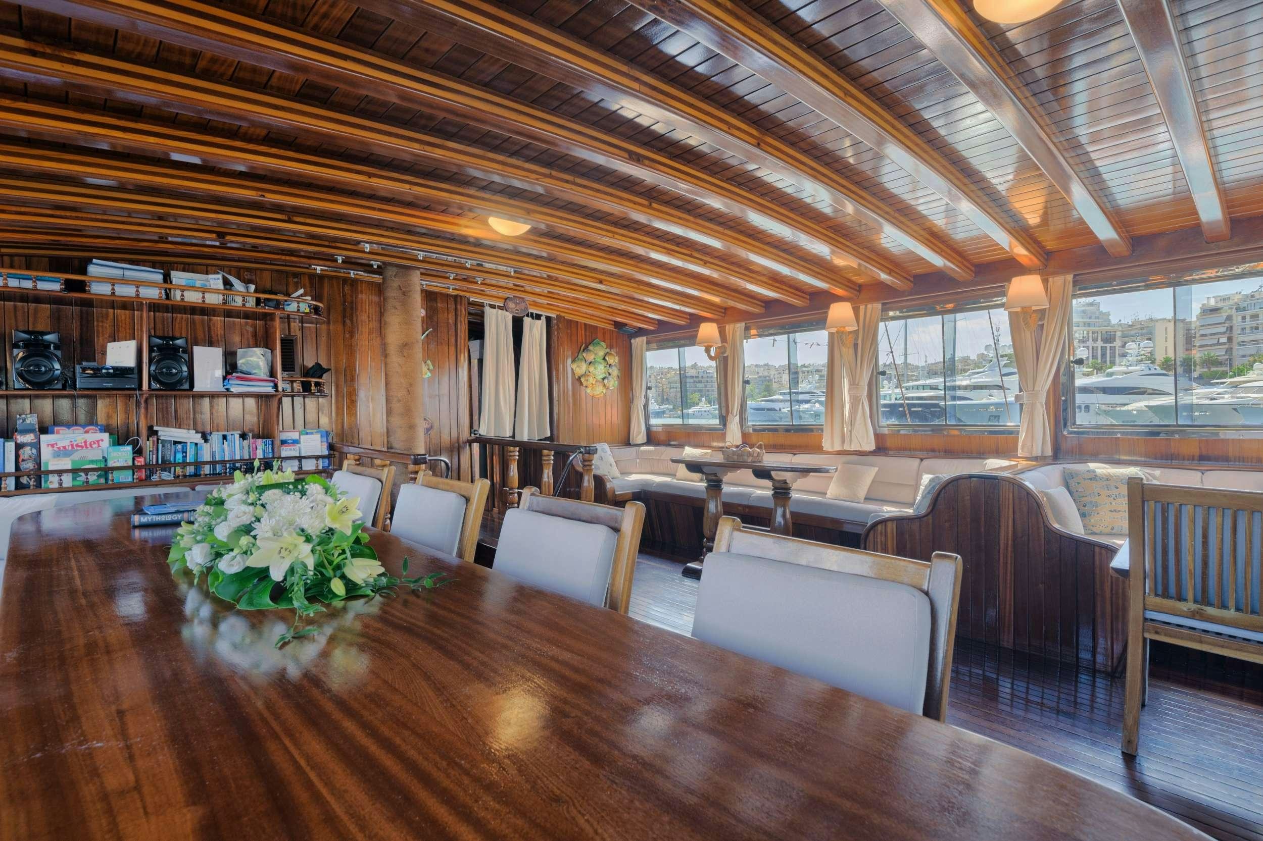 a room with a wood floor and a large wood table with chairs and a large window with a aboard THALASSA Yacht for Charter