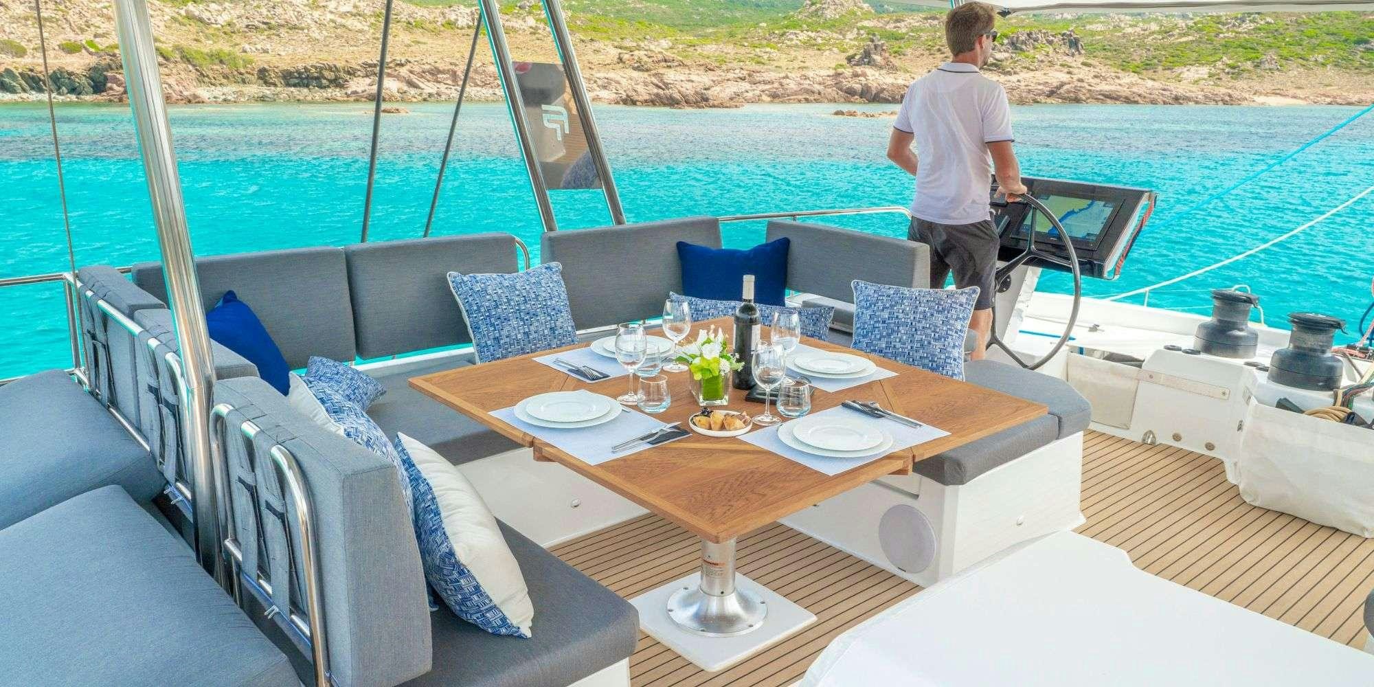 a person standing on a deck of a boat with a table and chairs aboard SEMPER FIDELIS Yacht for Charter