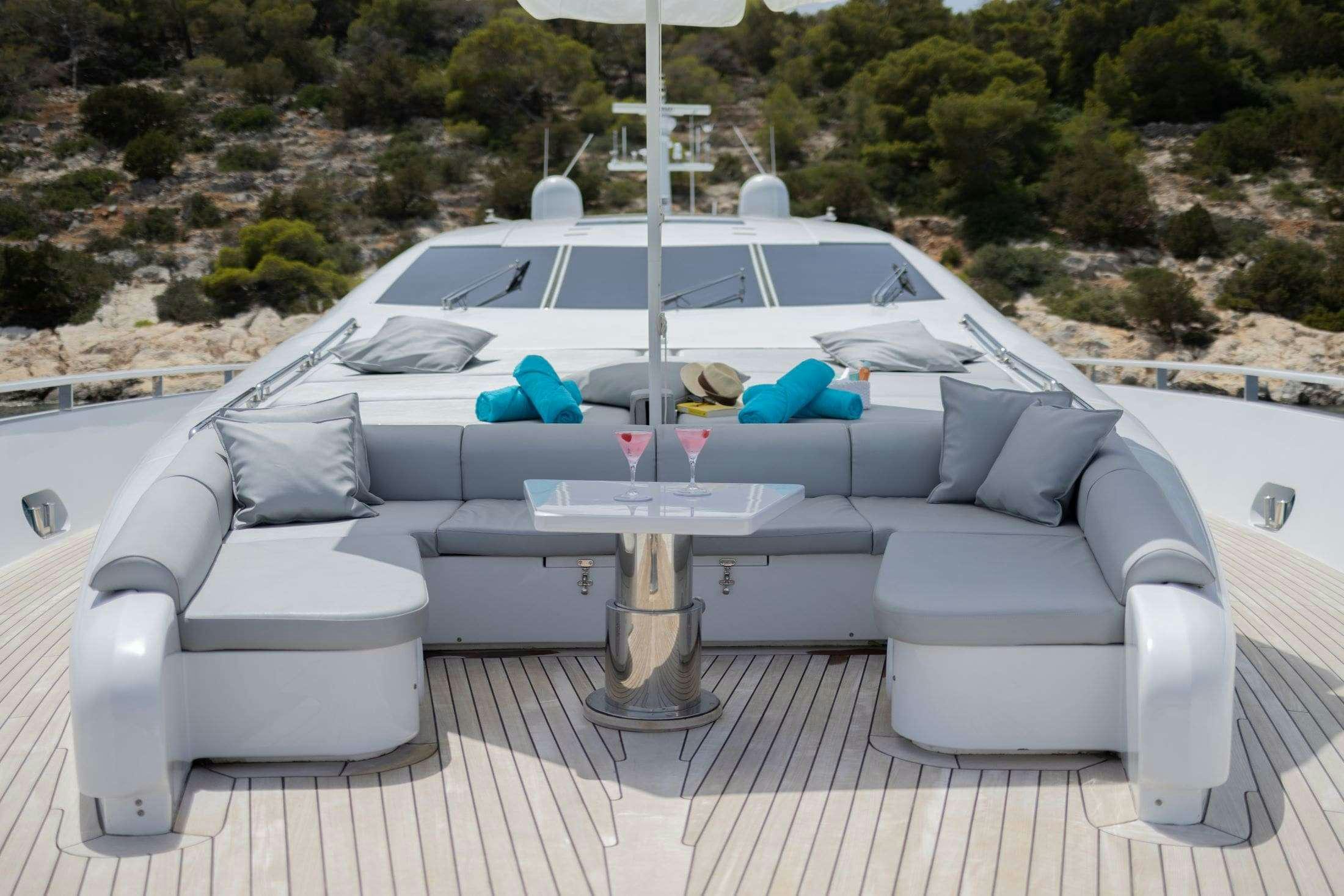 a white lounge chair with a table and a white sofa on a patio with trees and a hill aboard MAC Yacht for Charter