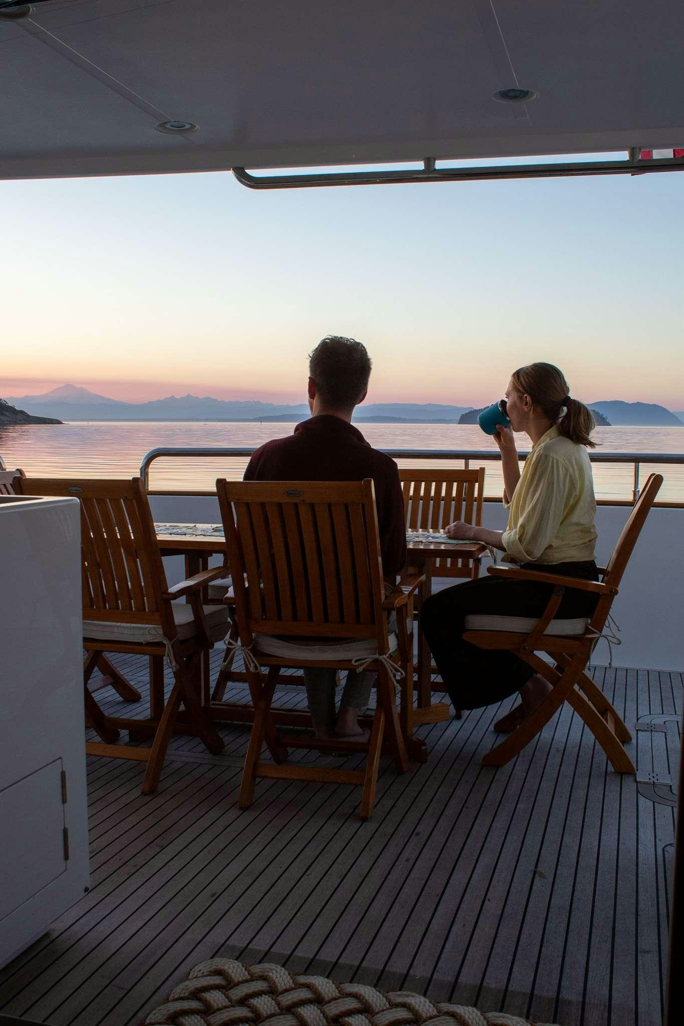 a man and woman sitting at a table on a deck overlooking the ocean aboard SERENDIPITY Yacht for Charter