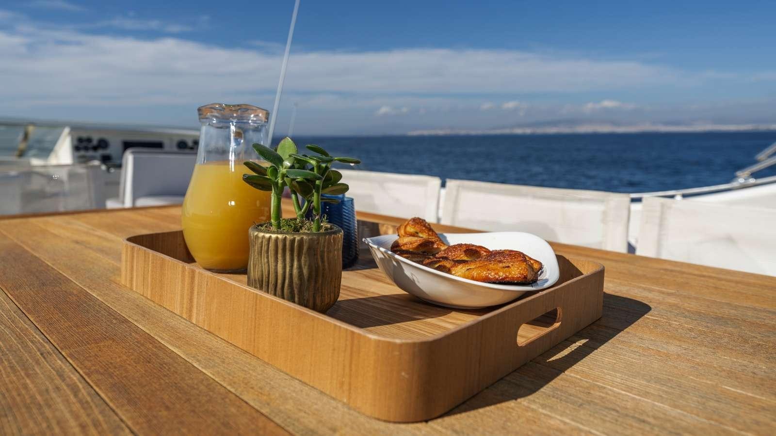 a table with a bowl of food and a glass of juice on a balcony overlooking the ocean aboard ALFA Yacht for Charter