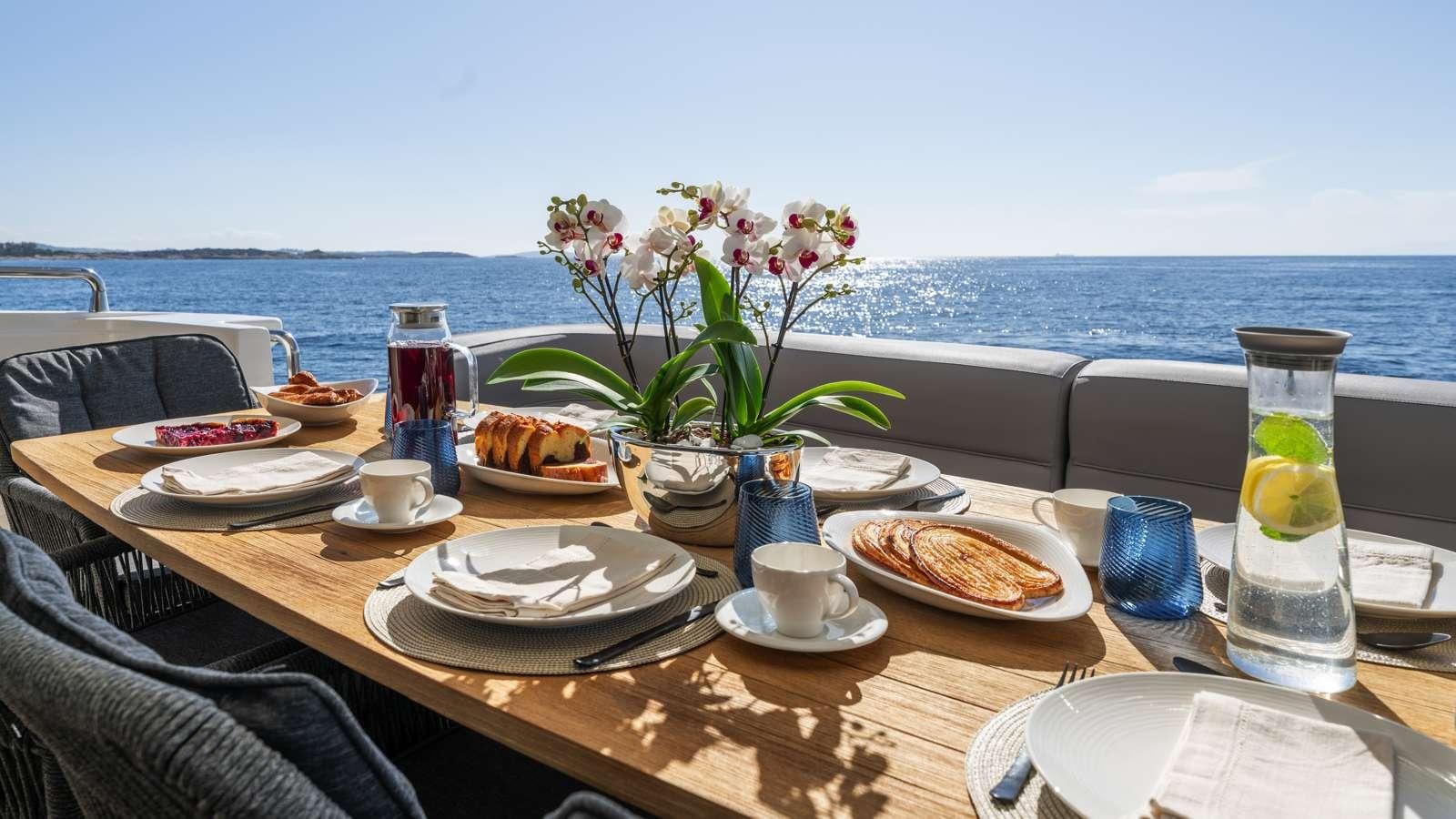 a table with plates and cups on it by the ocean aboard ALFA Yacht for Charter