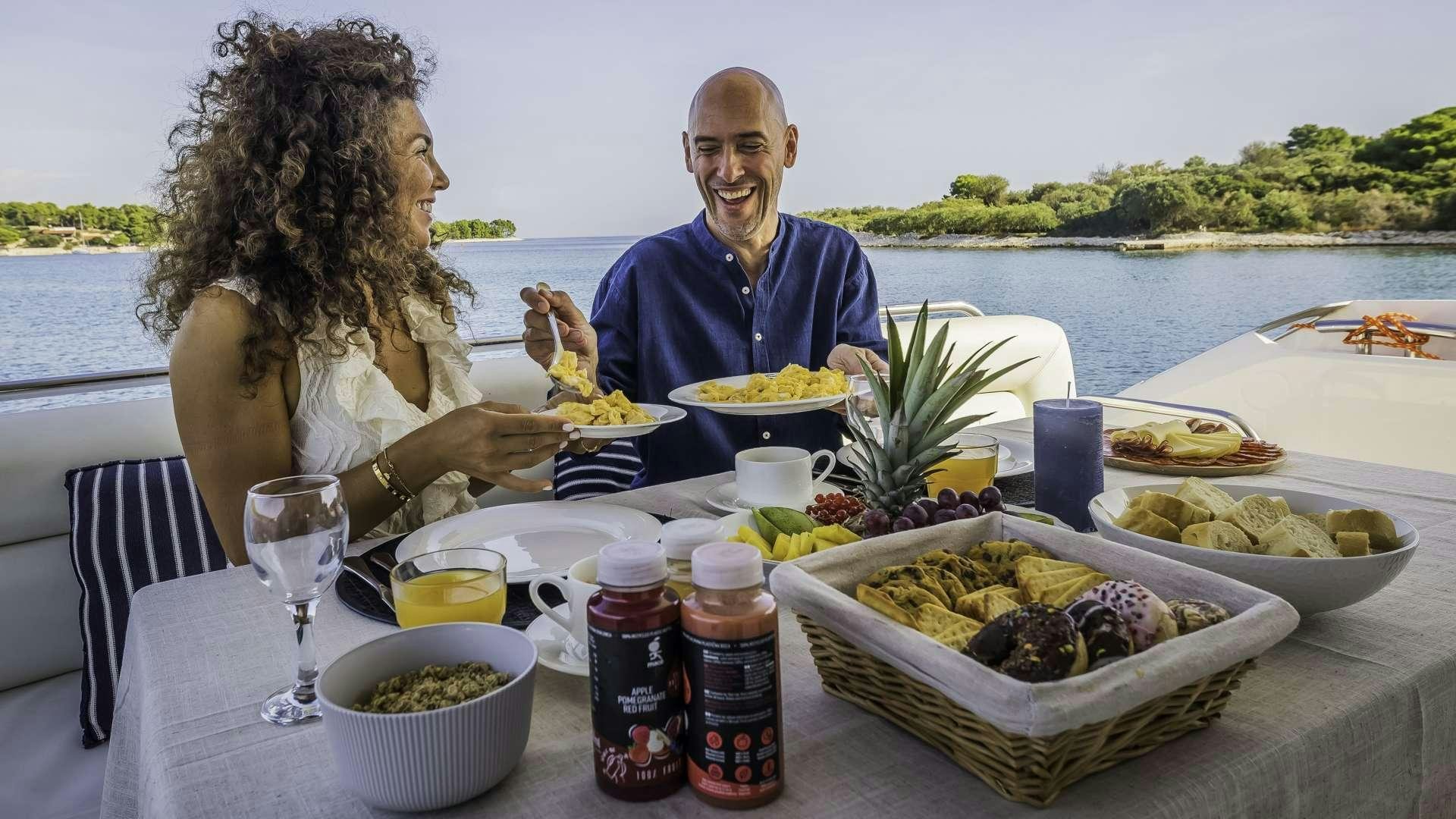 a man and woman eating at a table with a large body of water in the background aboard 2 DRUNK Yacht for Charter